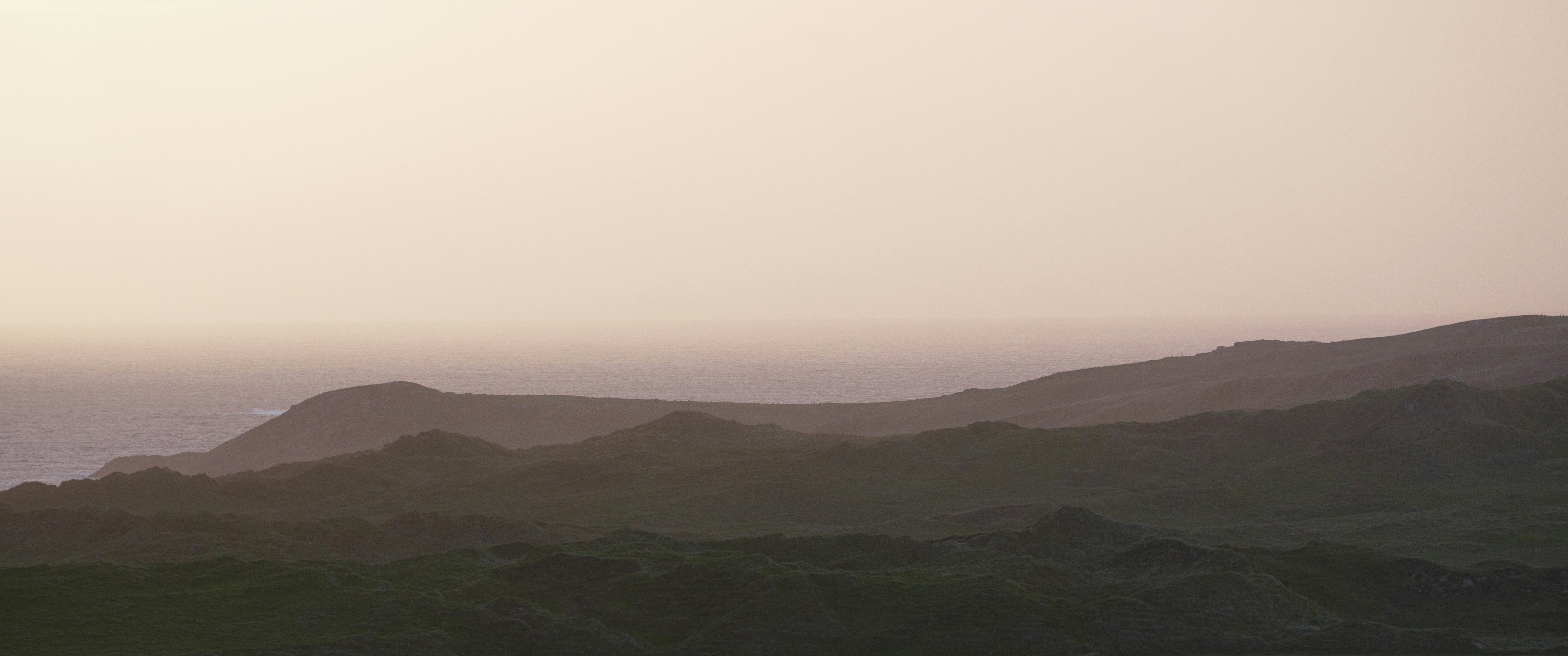 Mountains under a pale, cloudy sky at sunset.