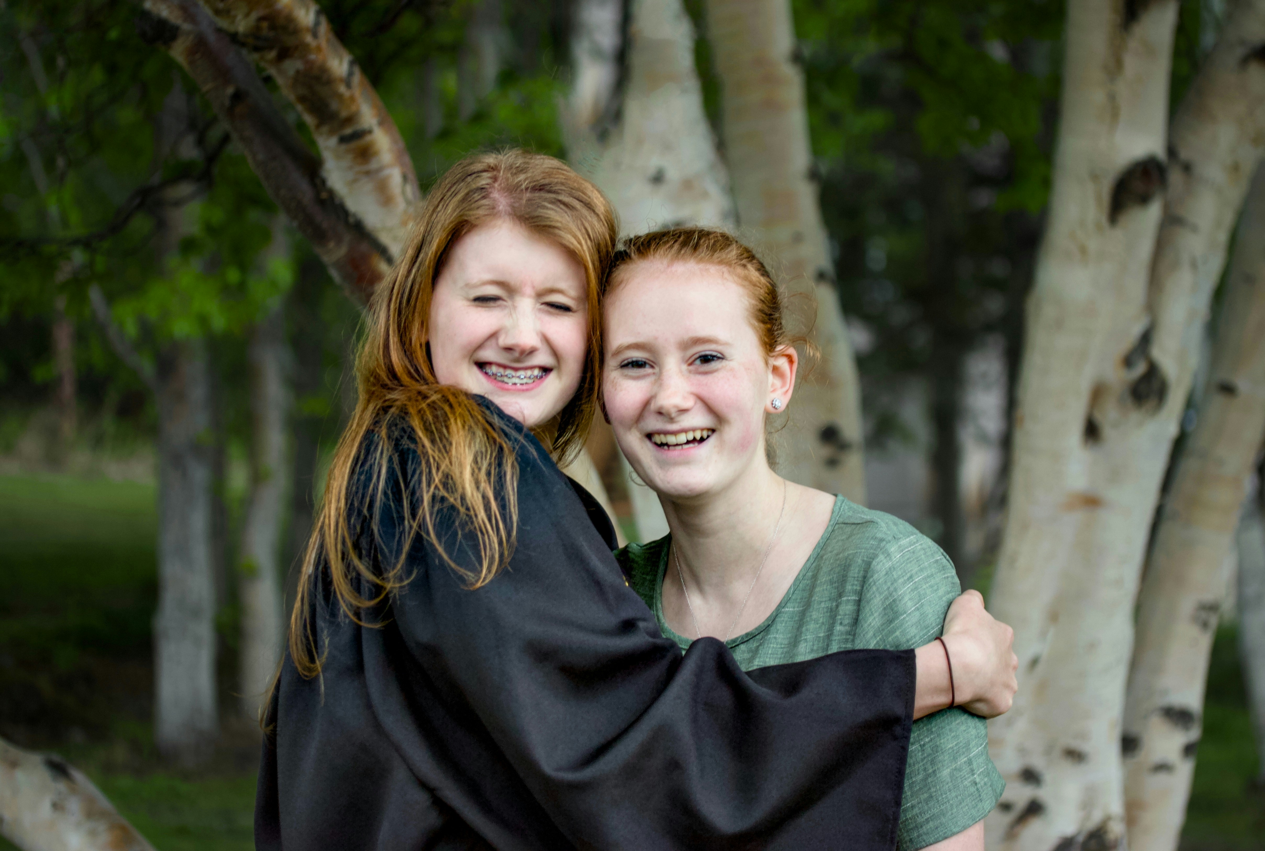 Two smiling girls are hugging each other outside.
