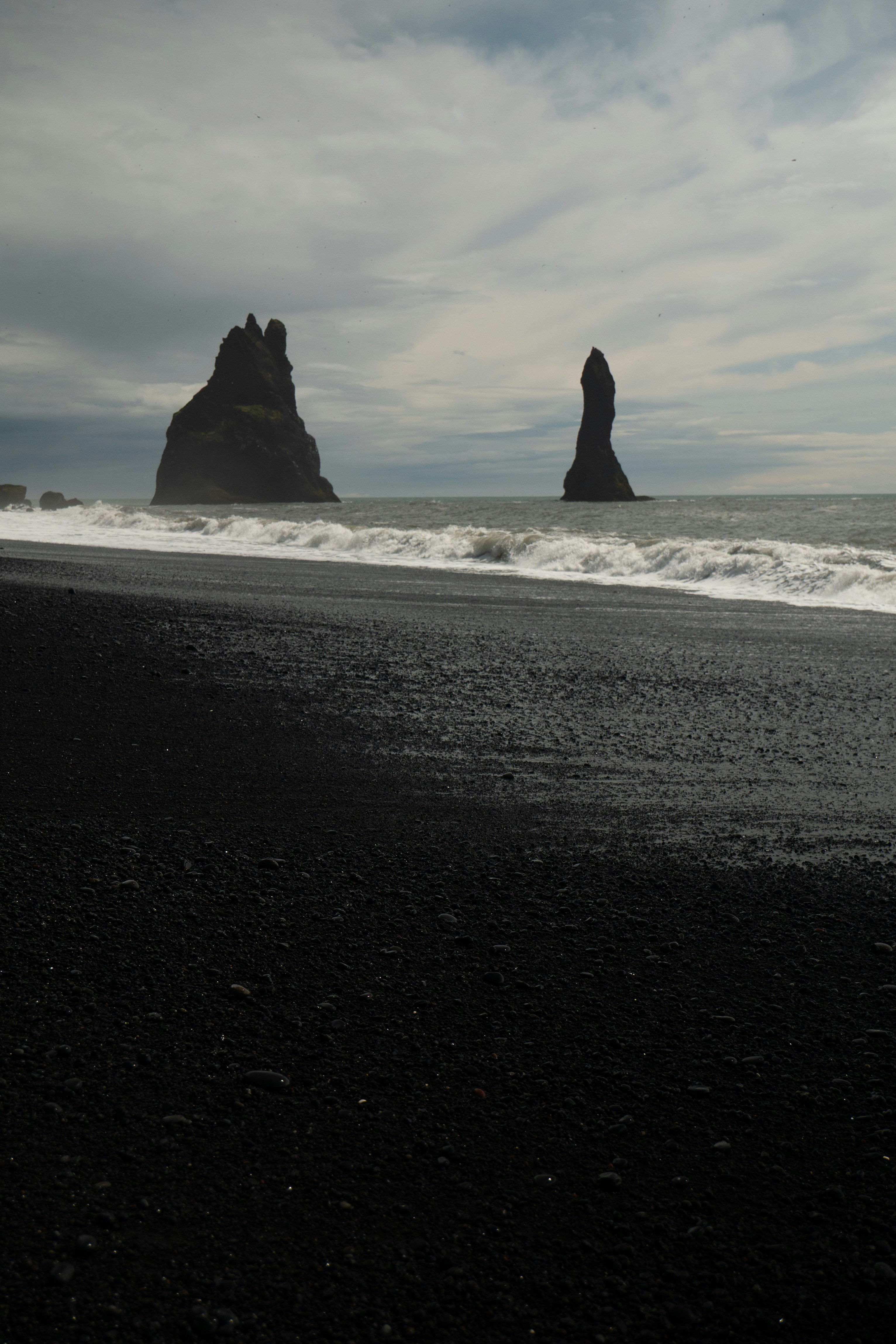 Black sand beach with rock formations in the ocean.