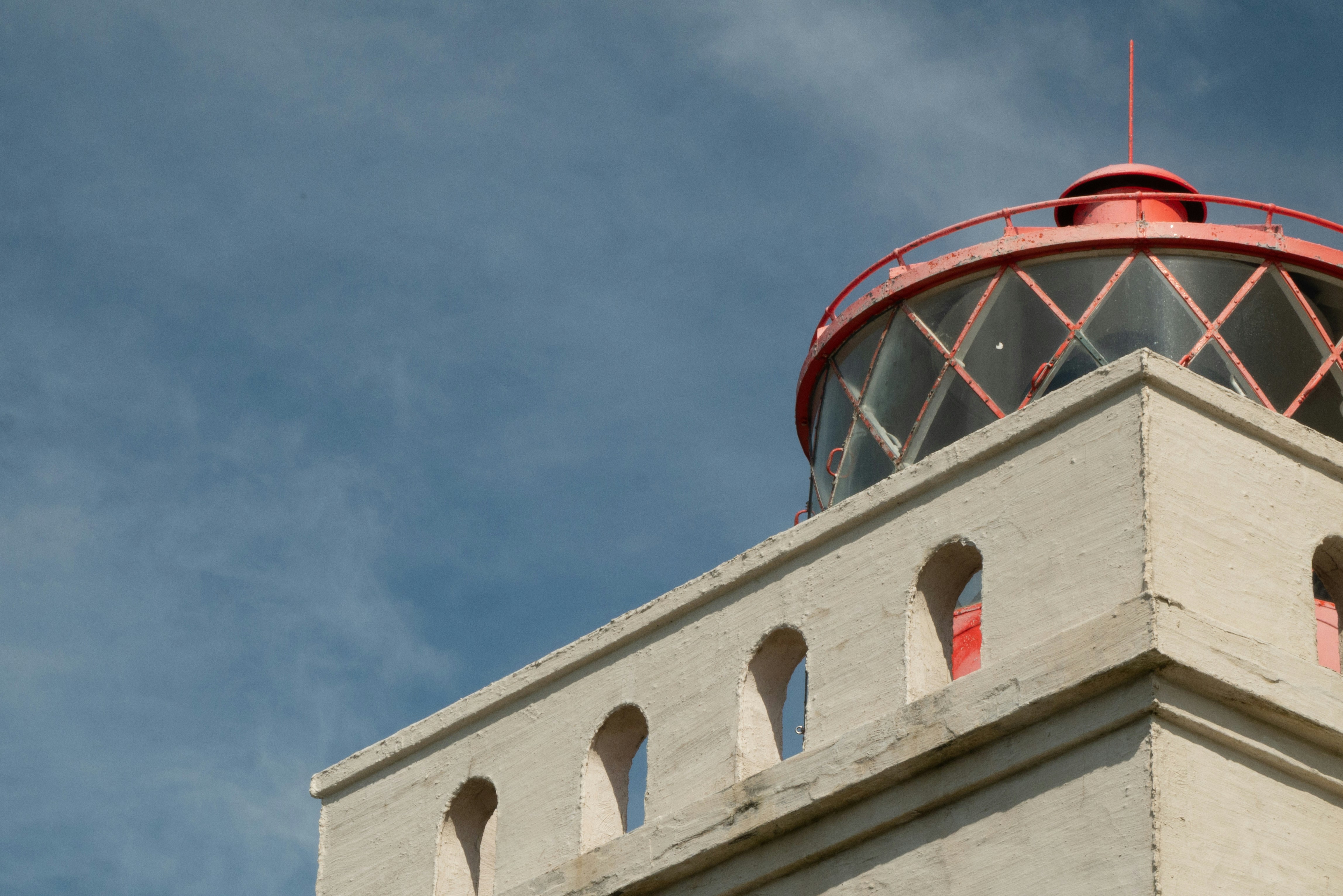 A lighthouse top under a cloudy, blue sky.
