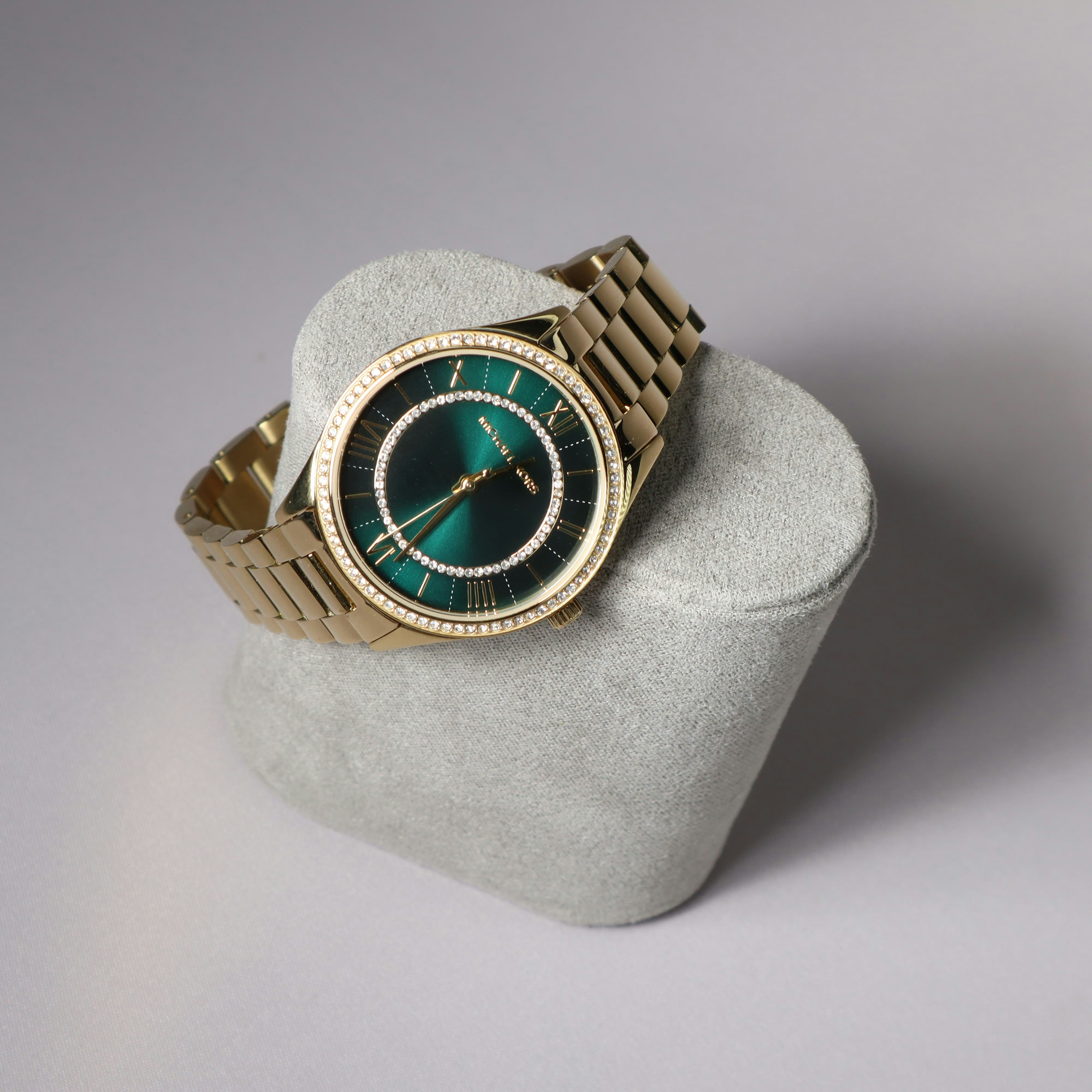 A gold watch displays its emerald green face.