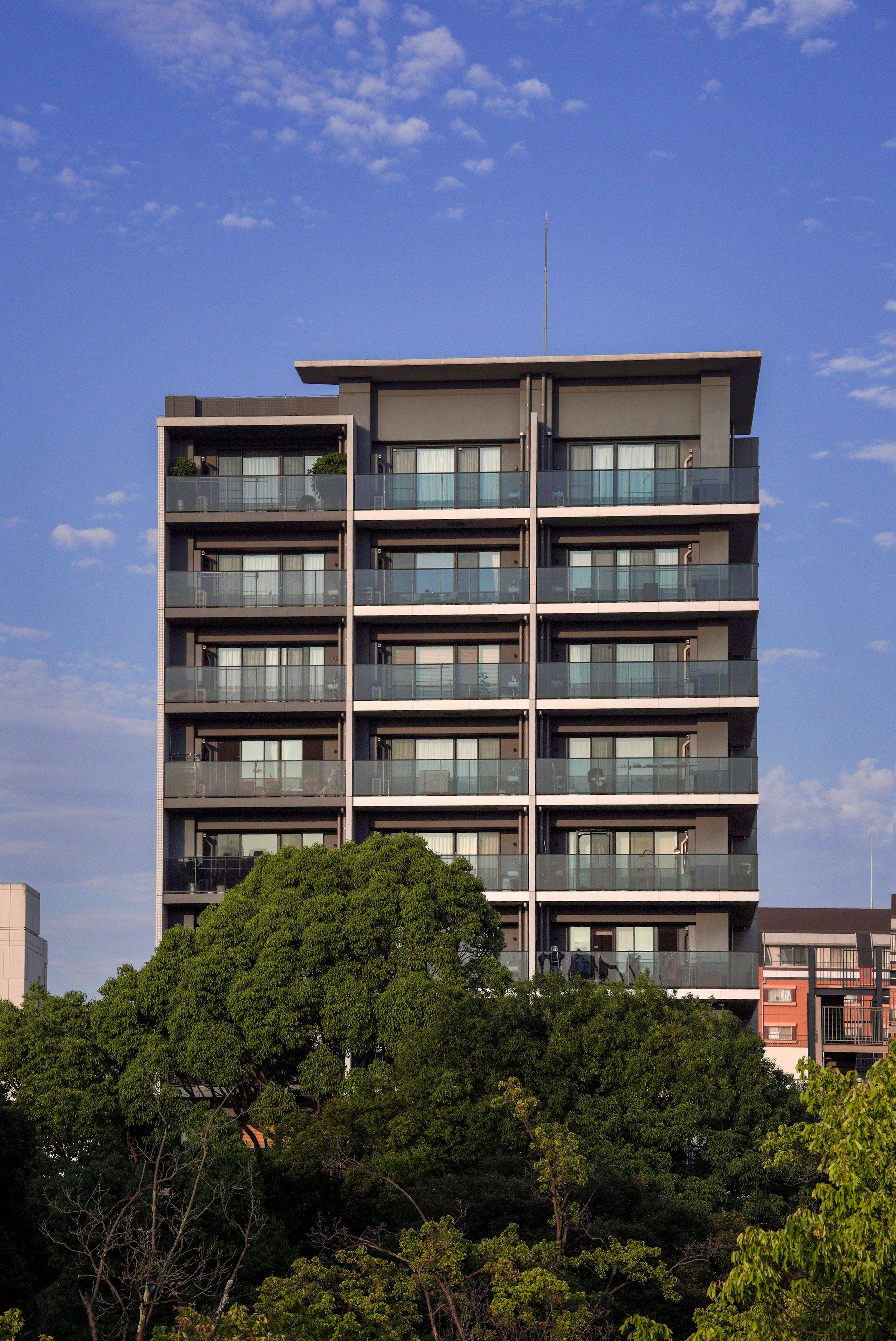 A modern apartment building rises above trees.