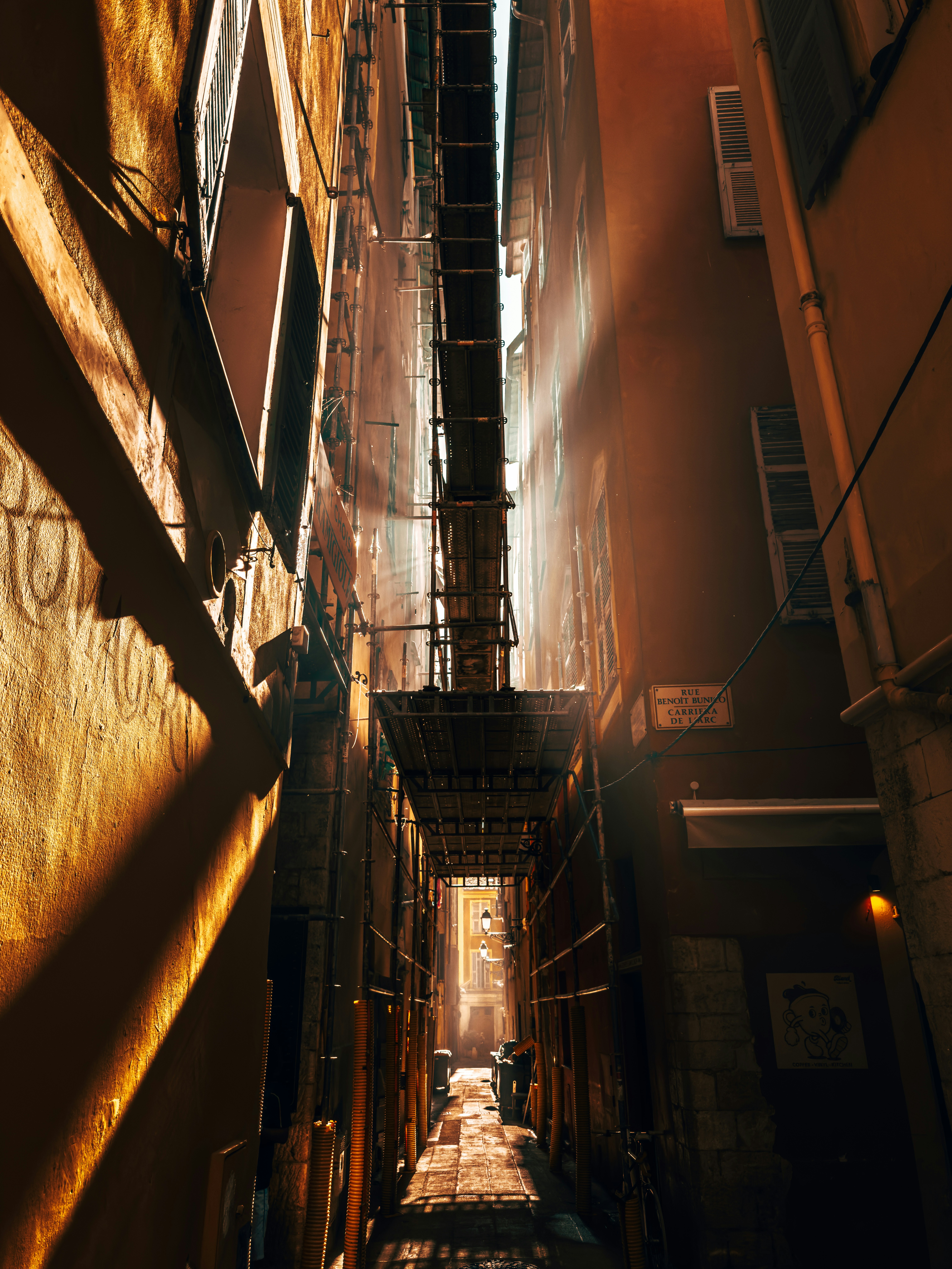 Schmale, sonnendurchflutete Gasse zwischen den Gebäuden.
