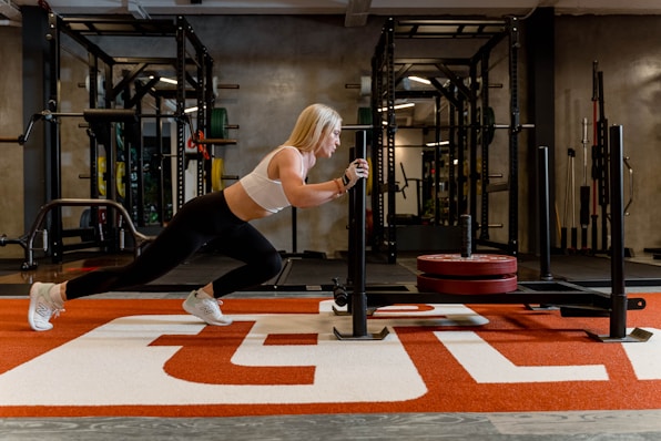 Woman is pushing a sled in a gym.