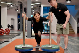 Woman performs exercise with trainer at gym.