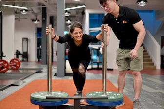 Woman performs exercise with trainer at gym.