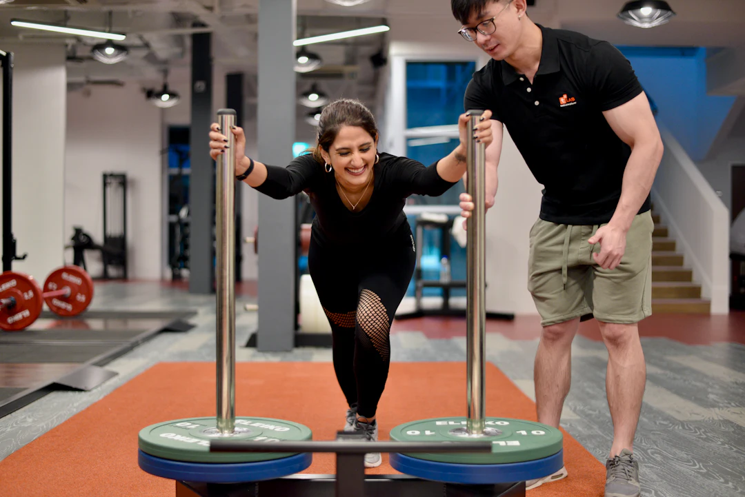 Aluna empurrando trenó na academia com o personal trainer ao lado