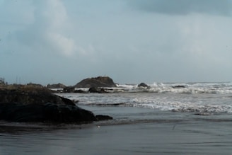 Waves crash on a rocky beach under a cloudy sky.
