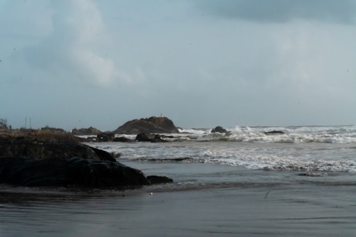 Waves crash on a rocky beach under a cloudy sky.