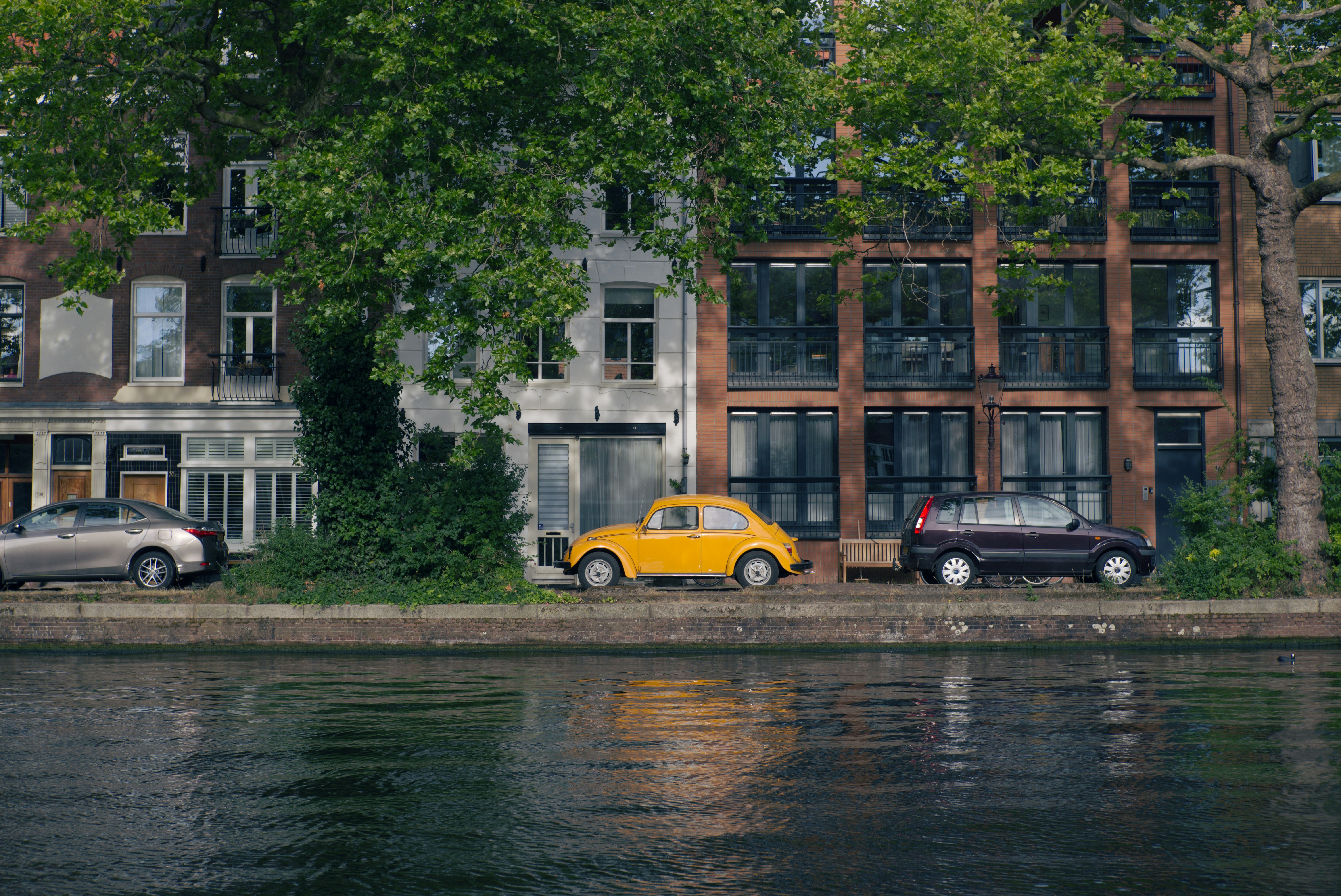 Cars parked along a canal near a building.