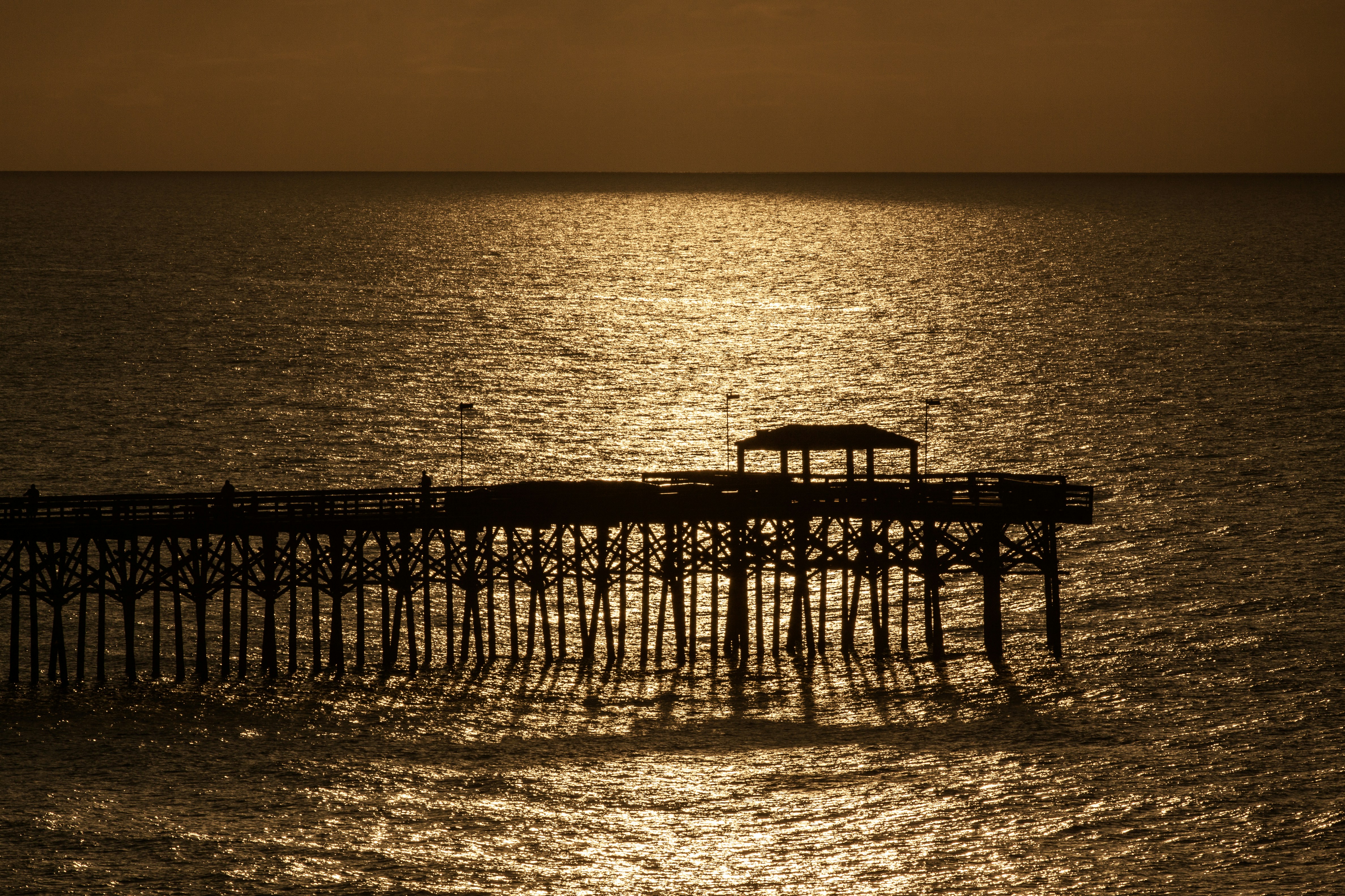 Pier silhouetted against the golden ocean.