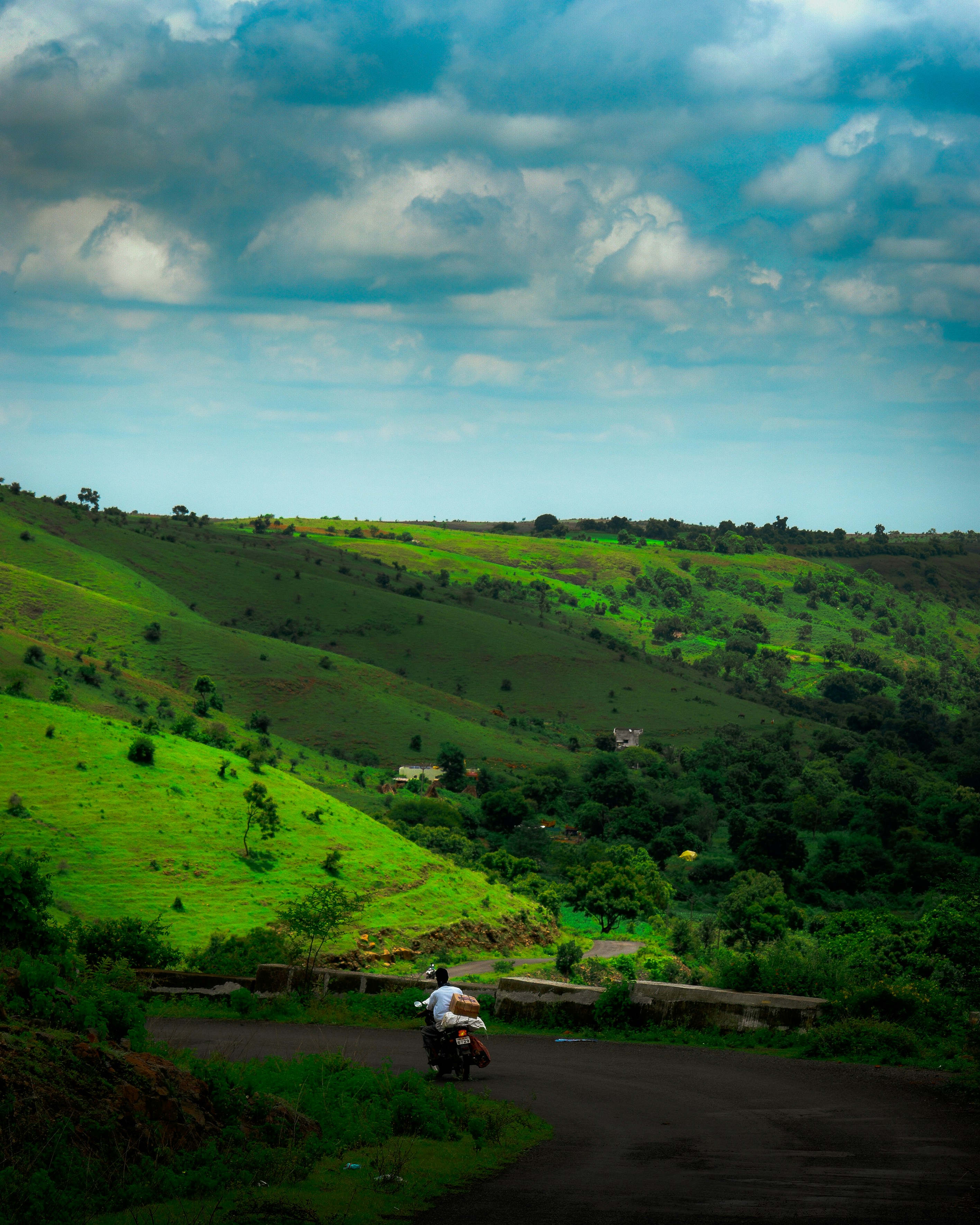 A motorcyclist rides on a road through green hills.