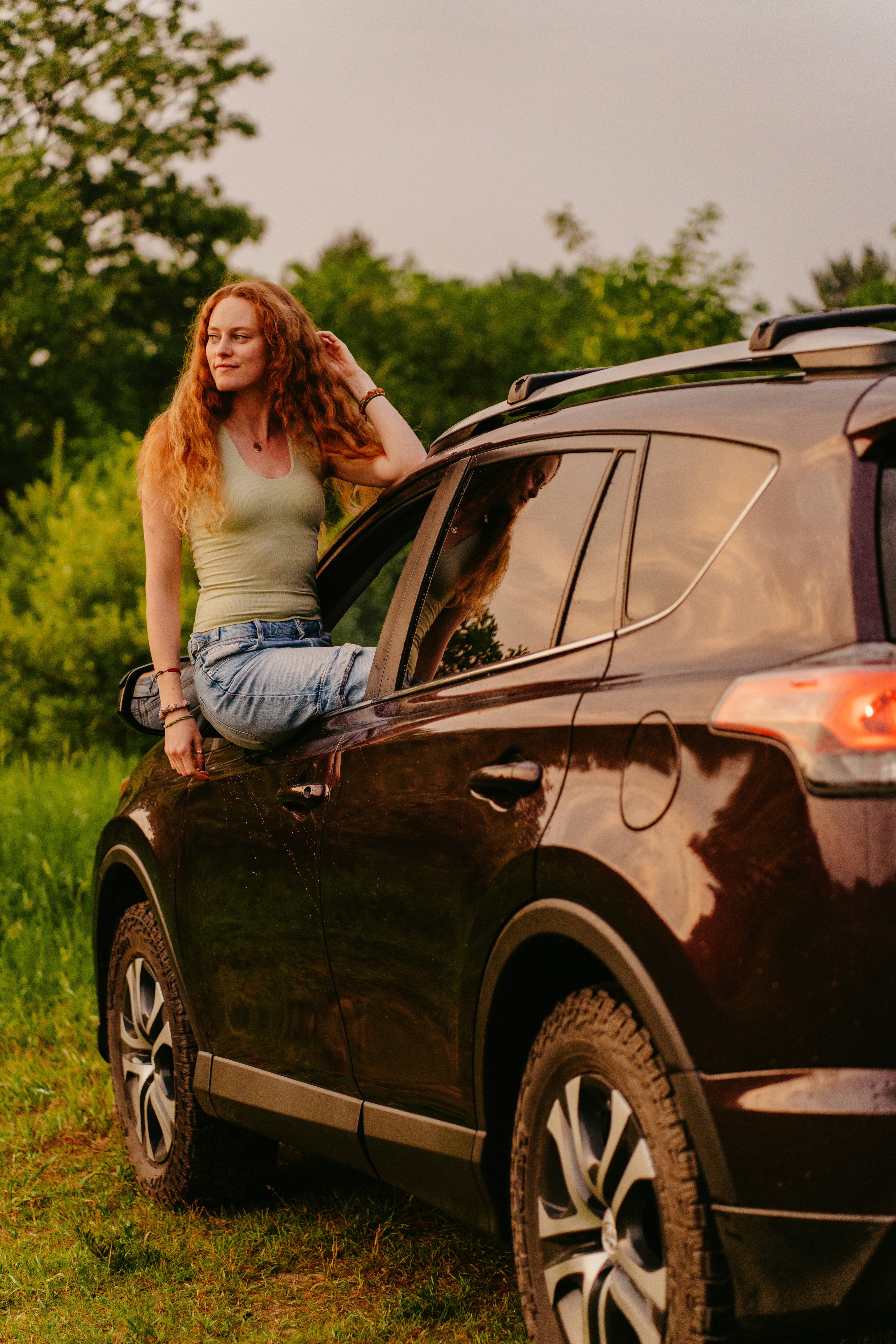 A red-haired woman sits on a dark suv.
