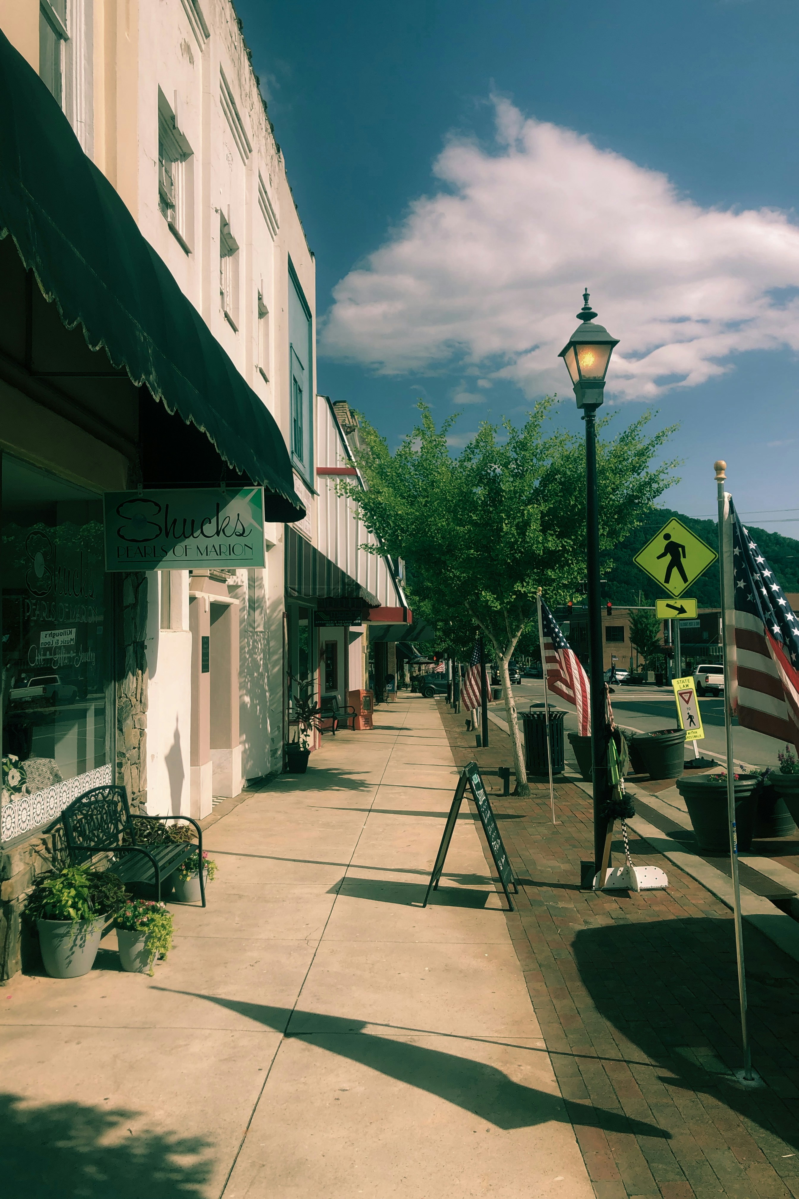 Une rue ensoleillée et calme avec des boutiques et des drapeaux.