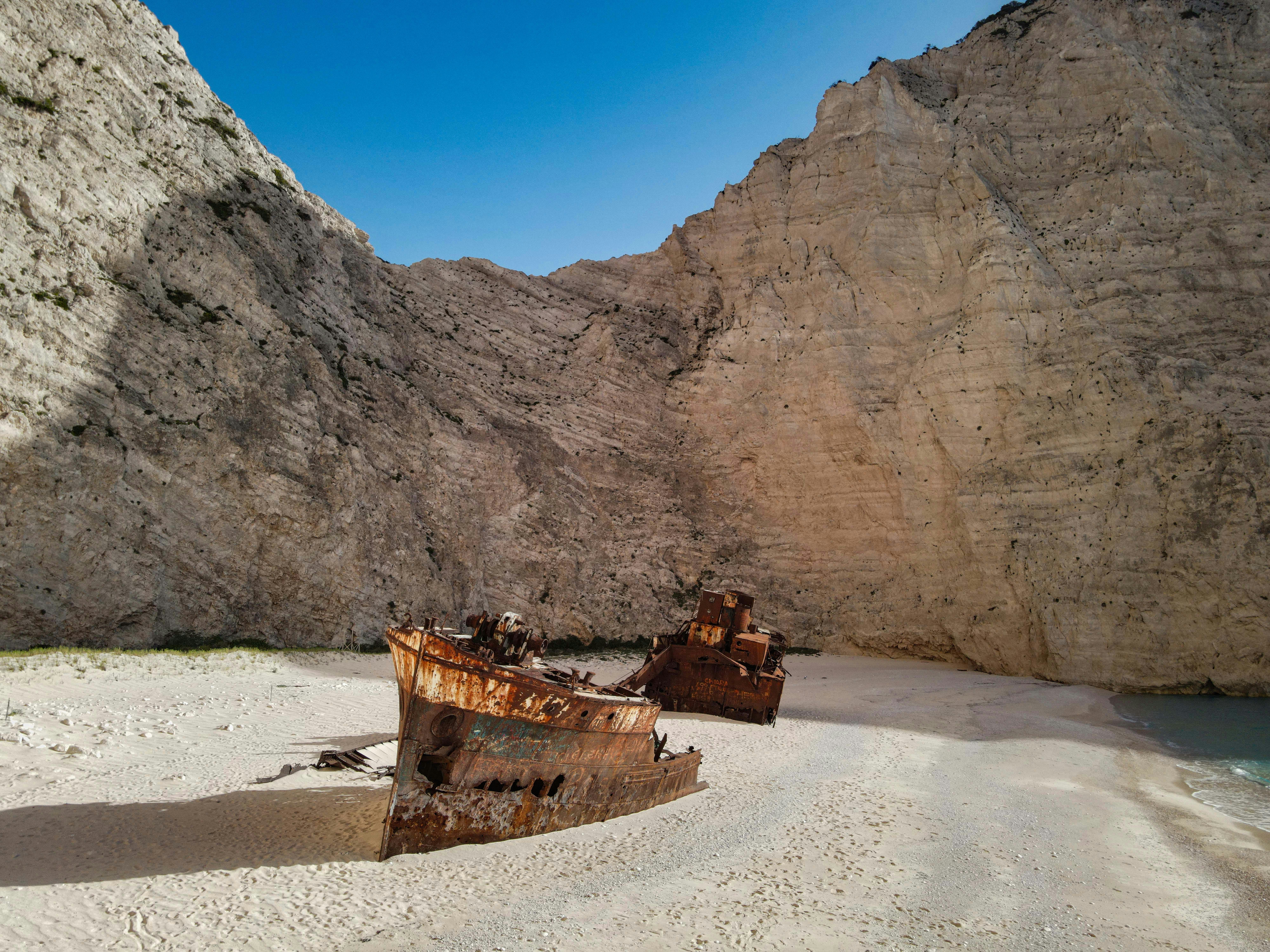 A shipwreck rests on a beach by cliffs