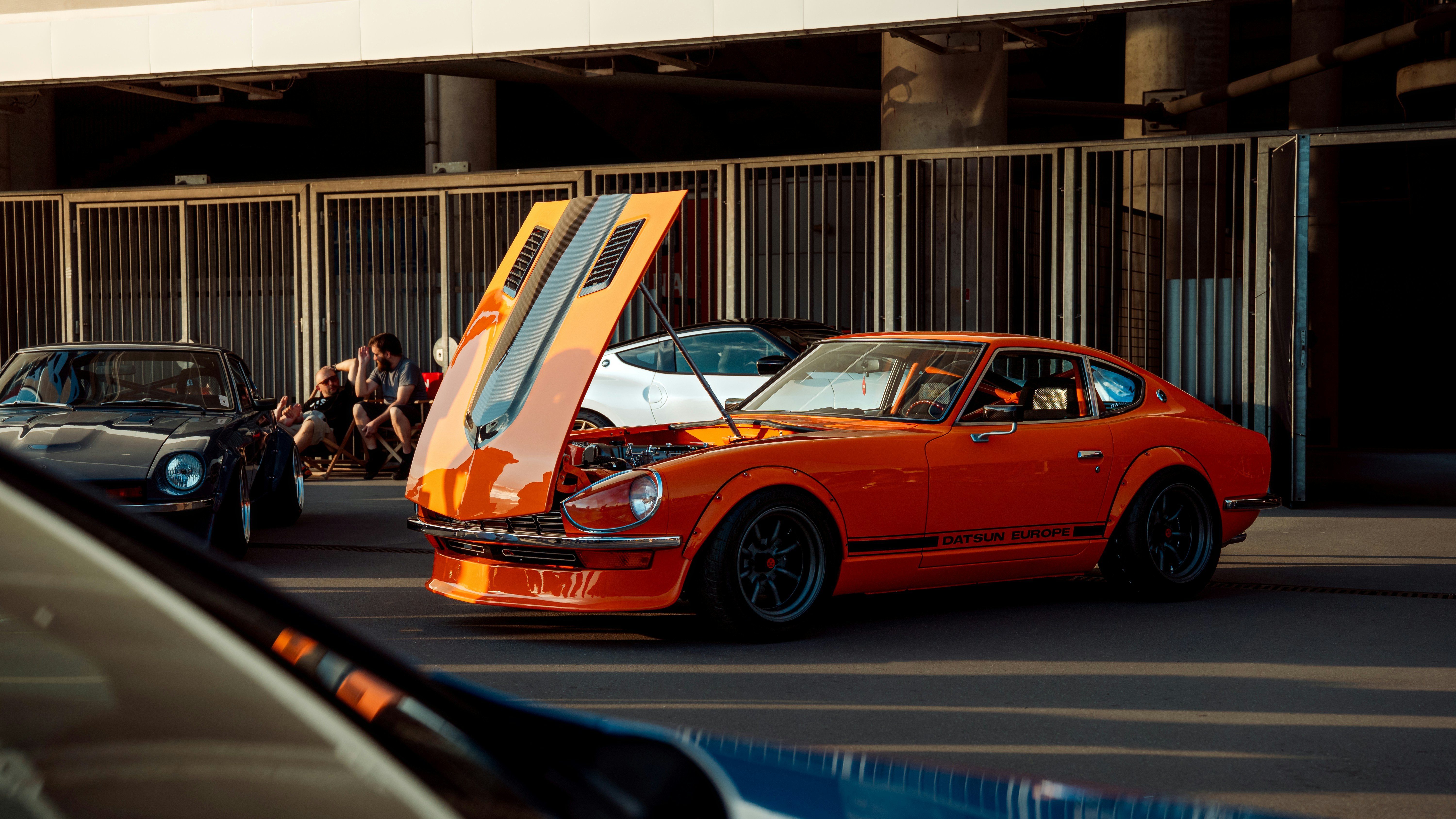 Orange car with its hood up in a parking lot.