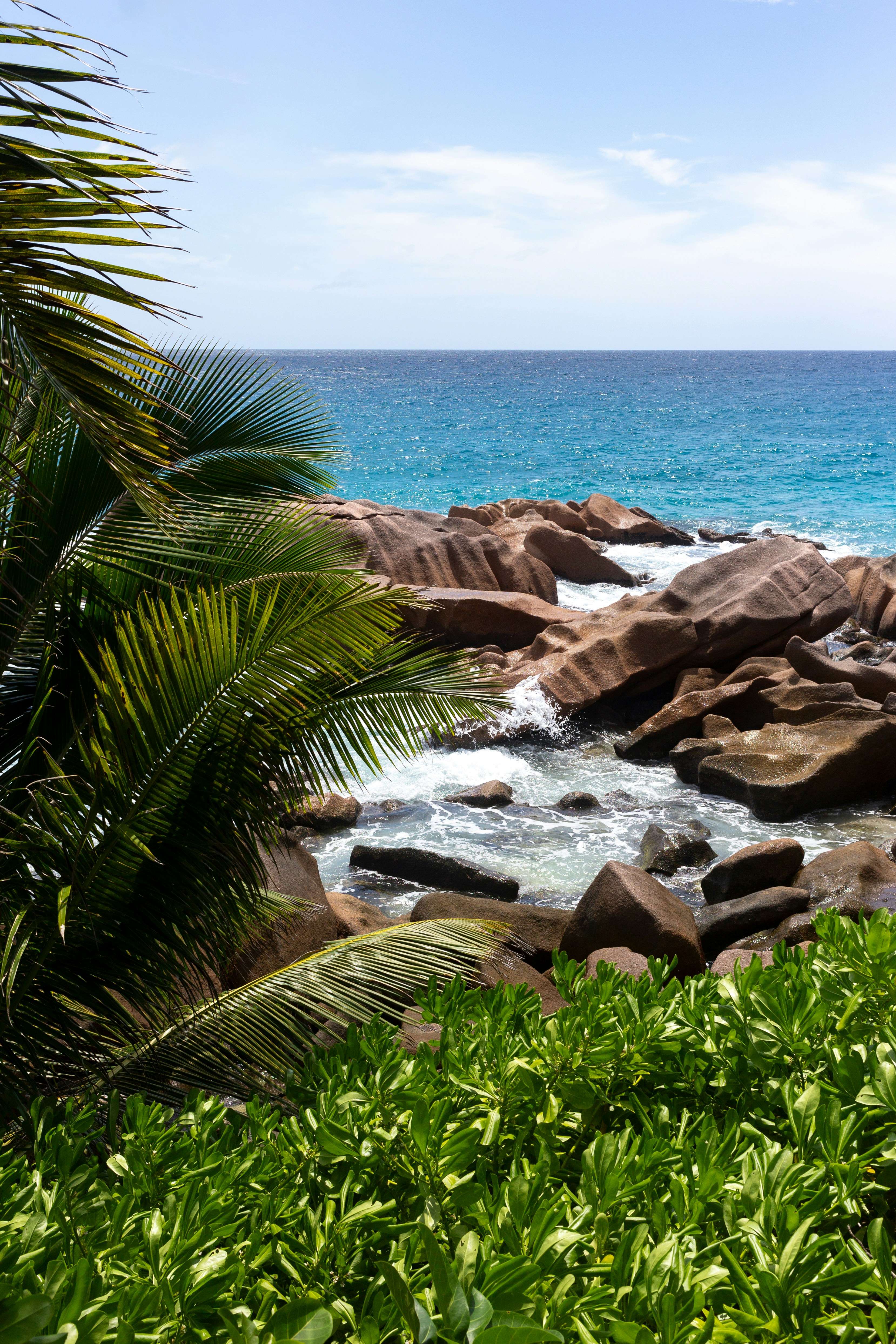 Ocean waves crash against rocks on a sunny day.