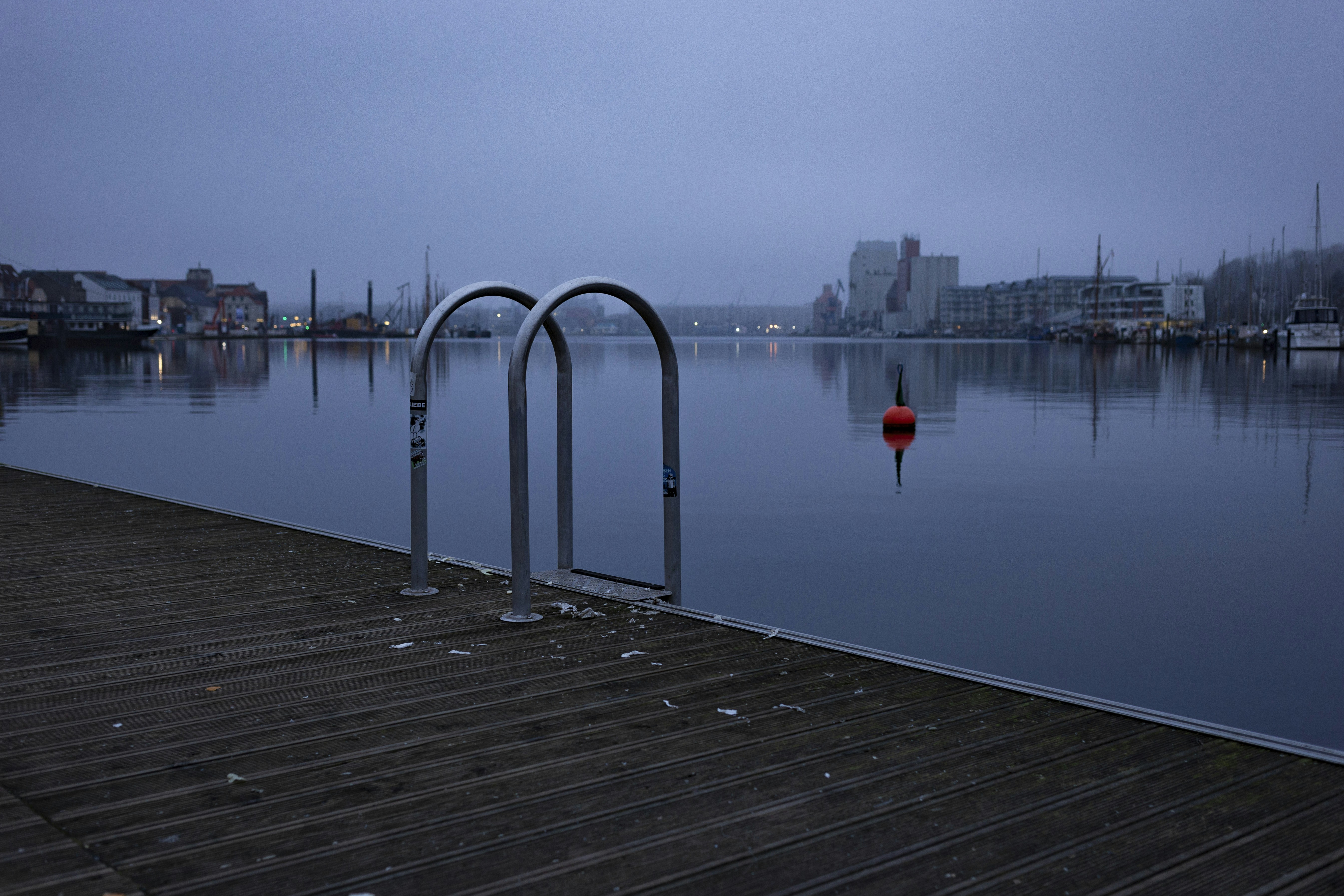 A calm harbor at dusk reflects city lights.