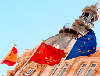 Flags wave in front of a historic building.