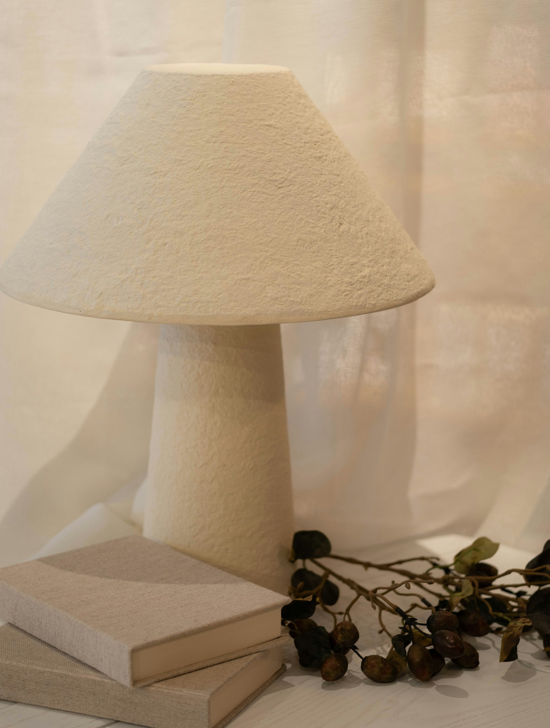 A lamp rests beside books and dried flowers.