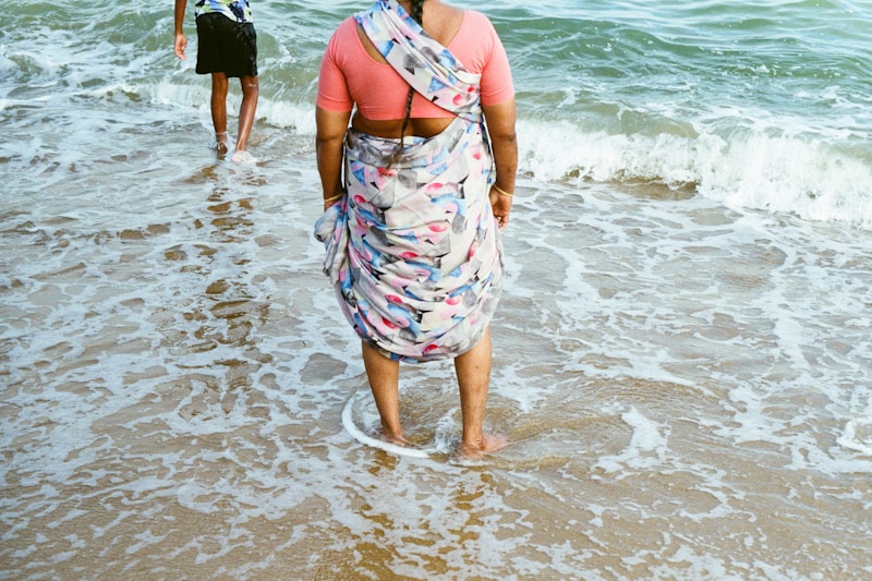 Woman wearing a sari stands at the ocean's edge.