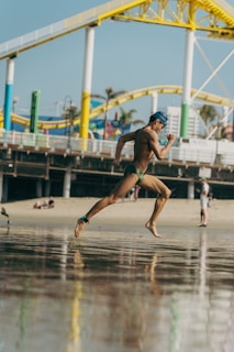Man runs on the beach near a pier.