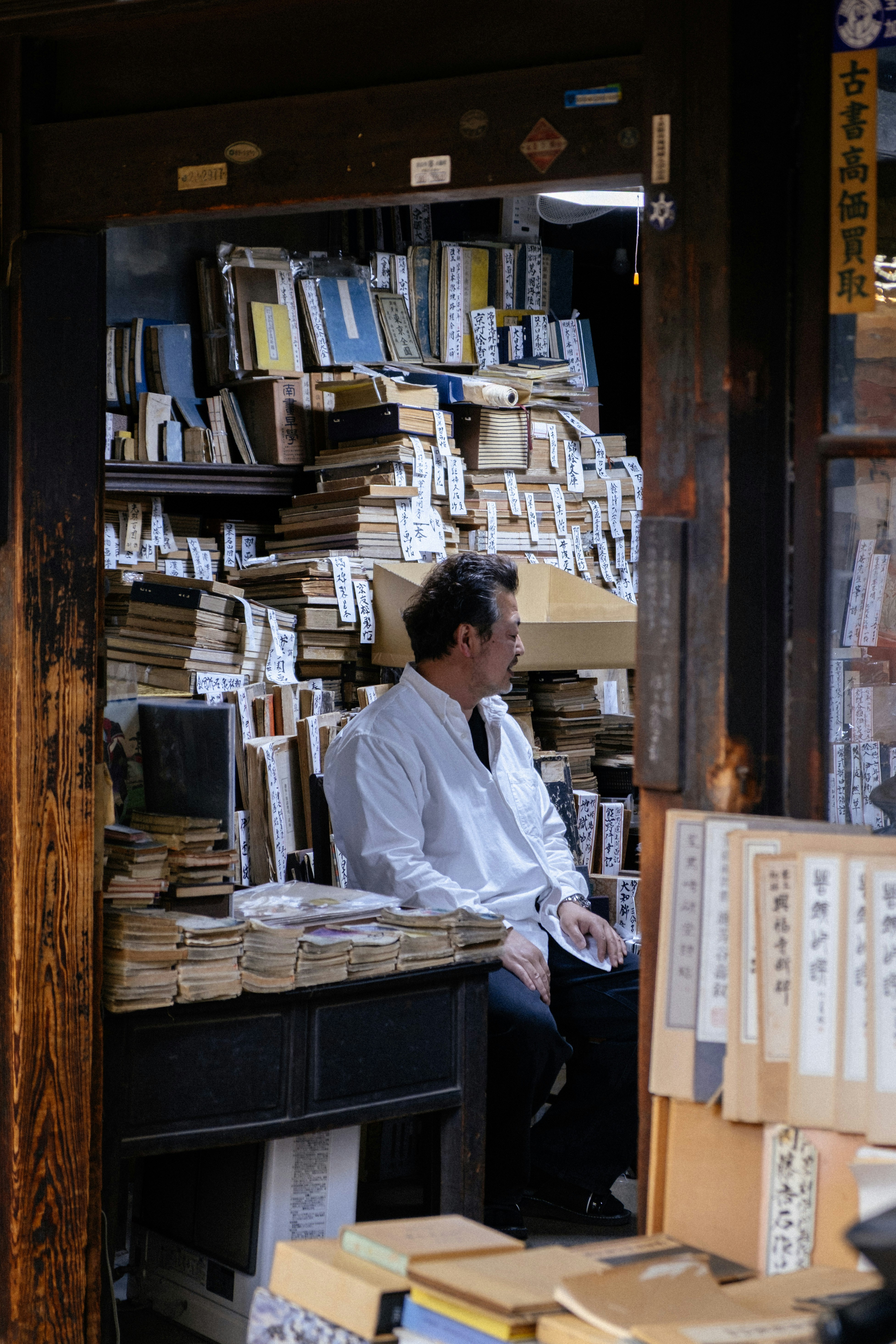 Man sits surrounded by stacks of old books.