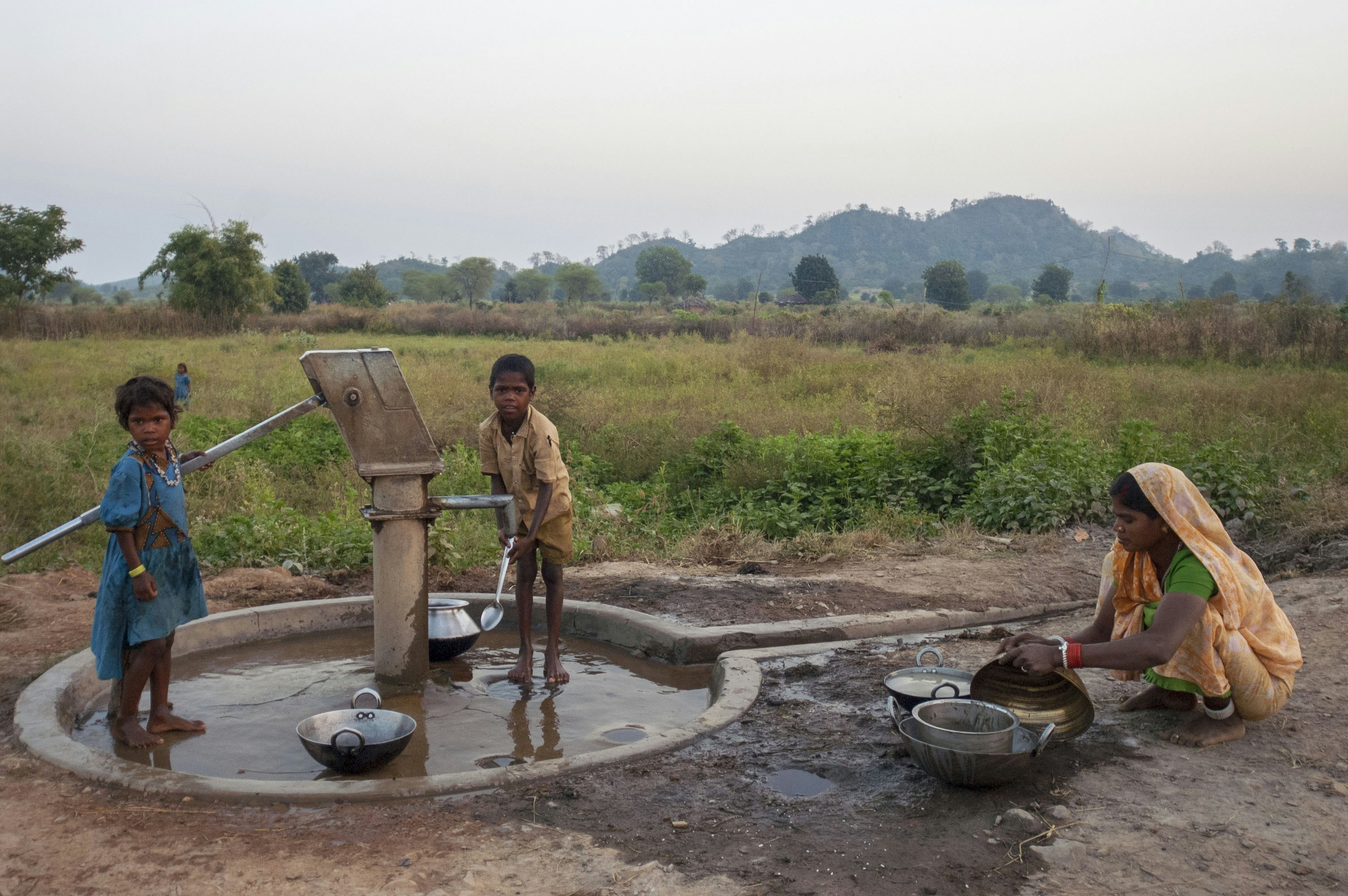 A dry handpump with a few villagers, including children, gathered around it looking dejected and helpless.