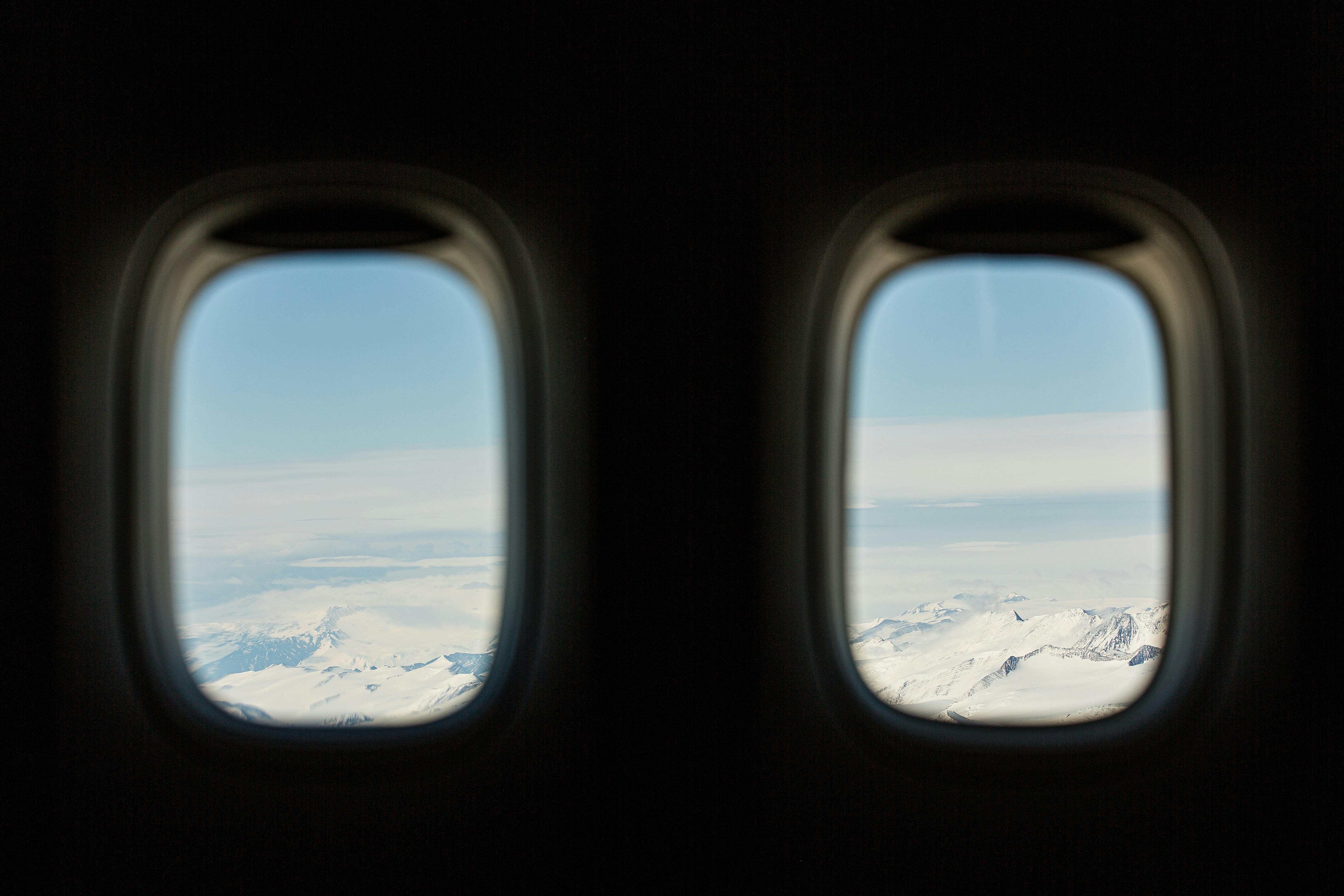 Two airplane windows reveal a snowy mountain landscape.