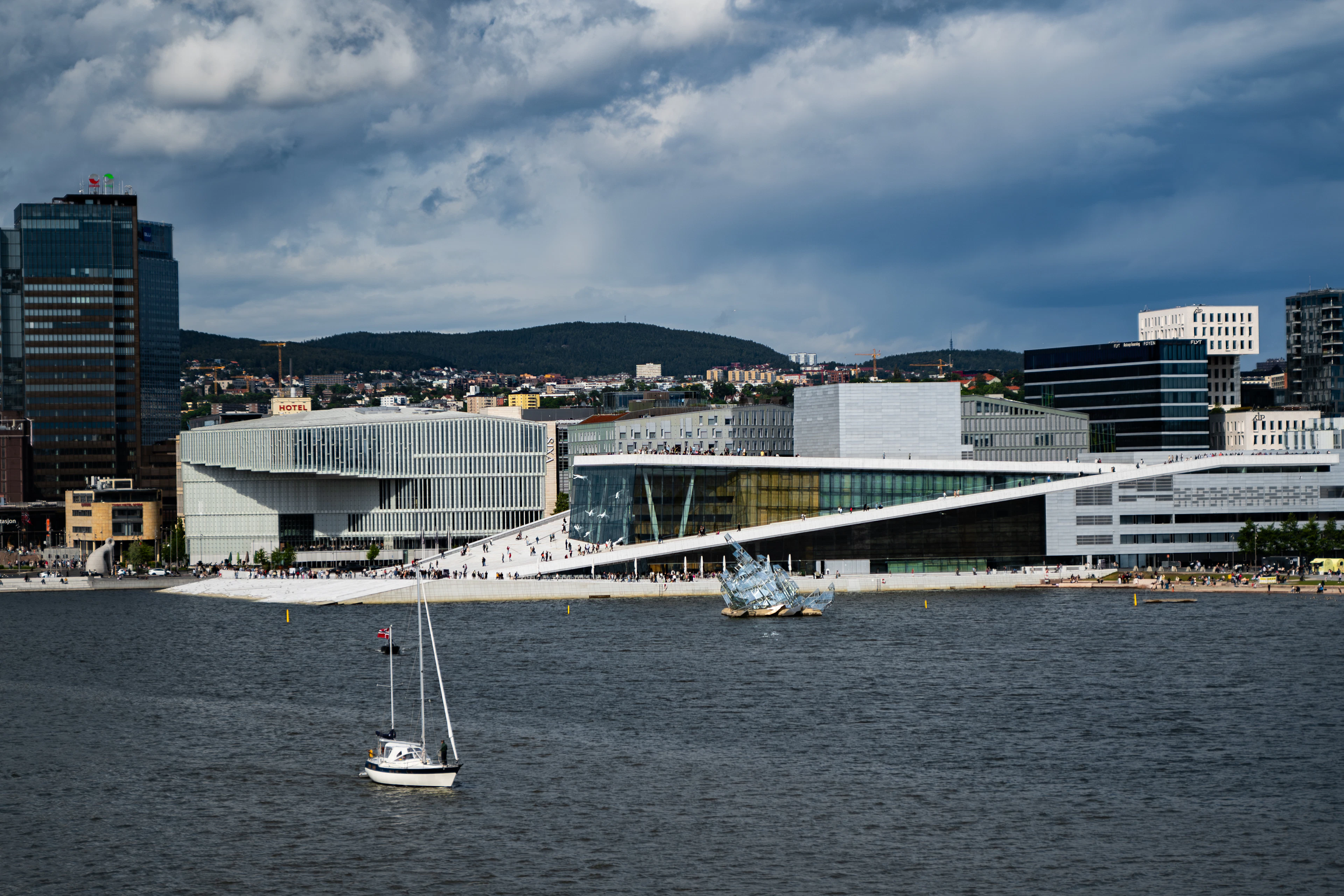 The white marble slopes of the Oslo Opera House on the waterfront, with sailboats on the fjord and the city skyline behind.
