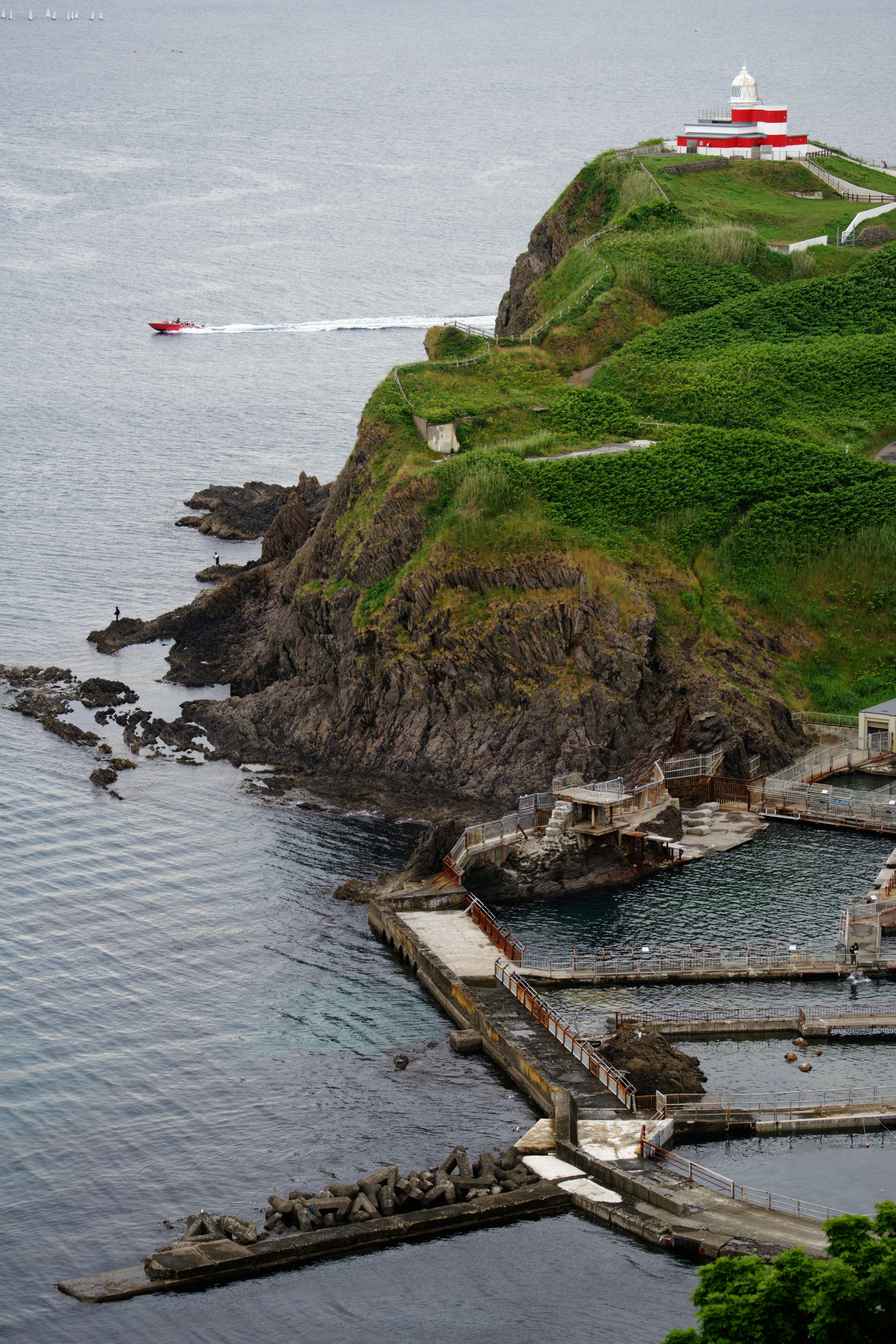 Lighthouse stands above pools near the ocean.