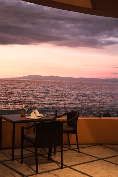 A romantic dinner table set on a terrace overlooking the ocean at sunset, evoking a cliffside dining terrace