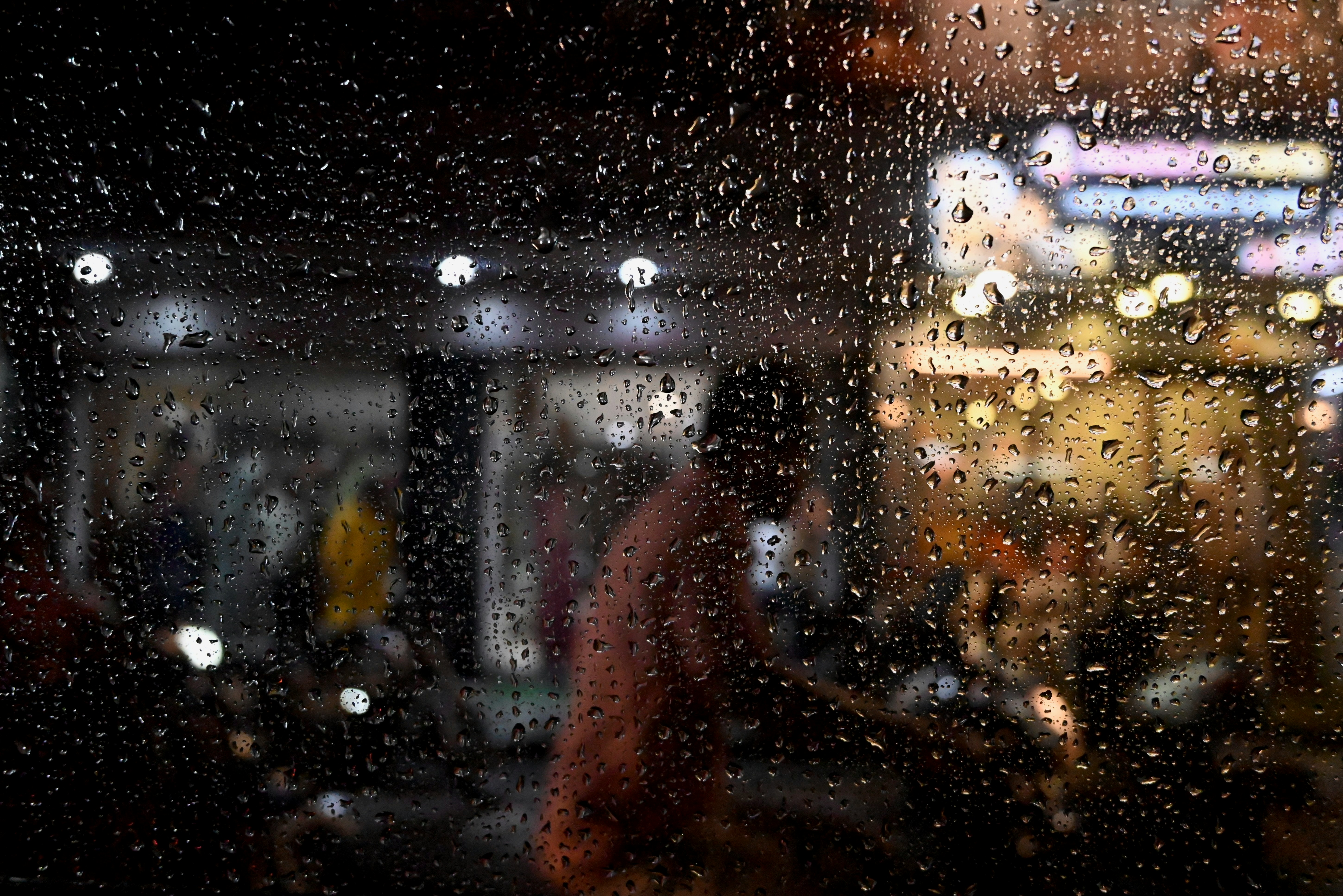 Gotas de chuva no vidro obscurecem uma cena urbana borrada.