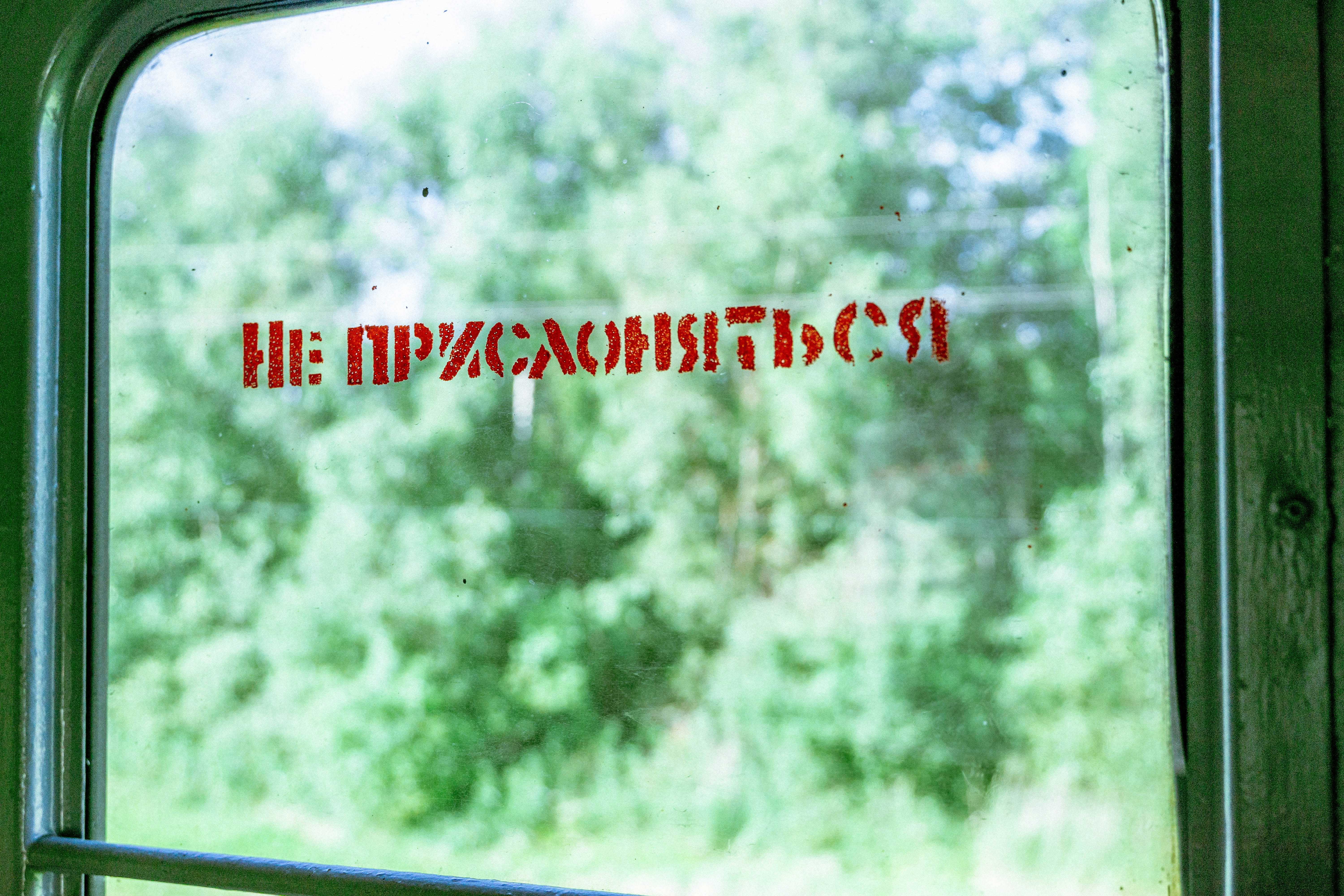 warning sign on old train window with blurry green trees outside view