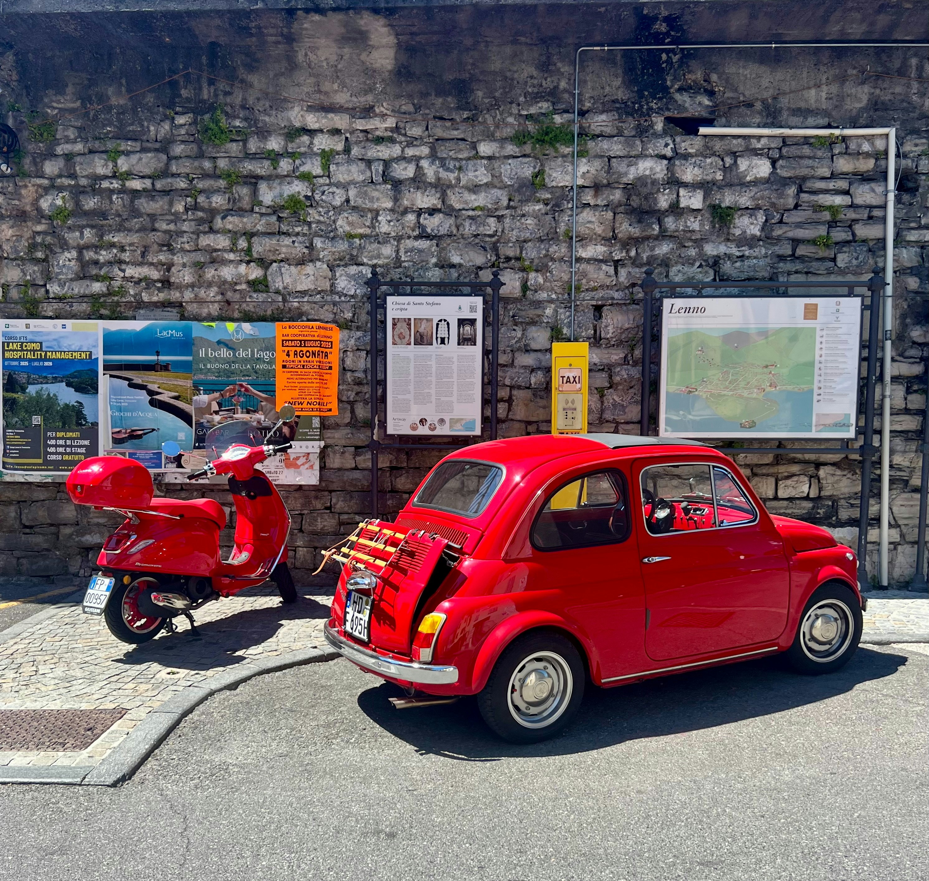 Red scooter and car parked near a stone wall.