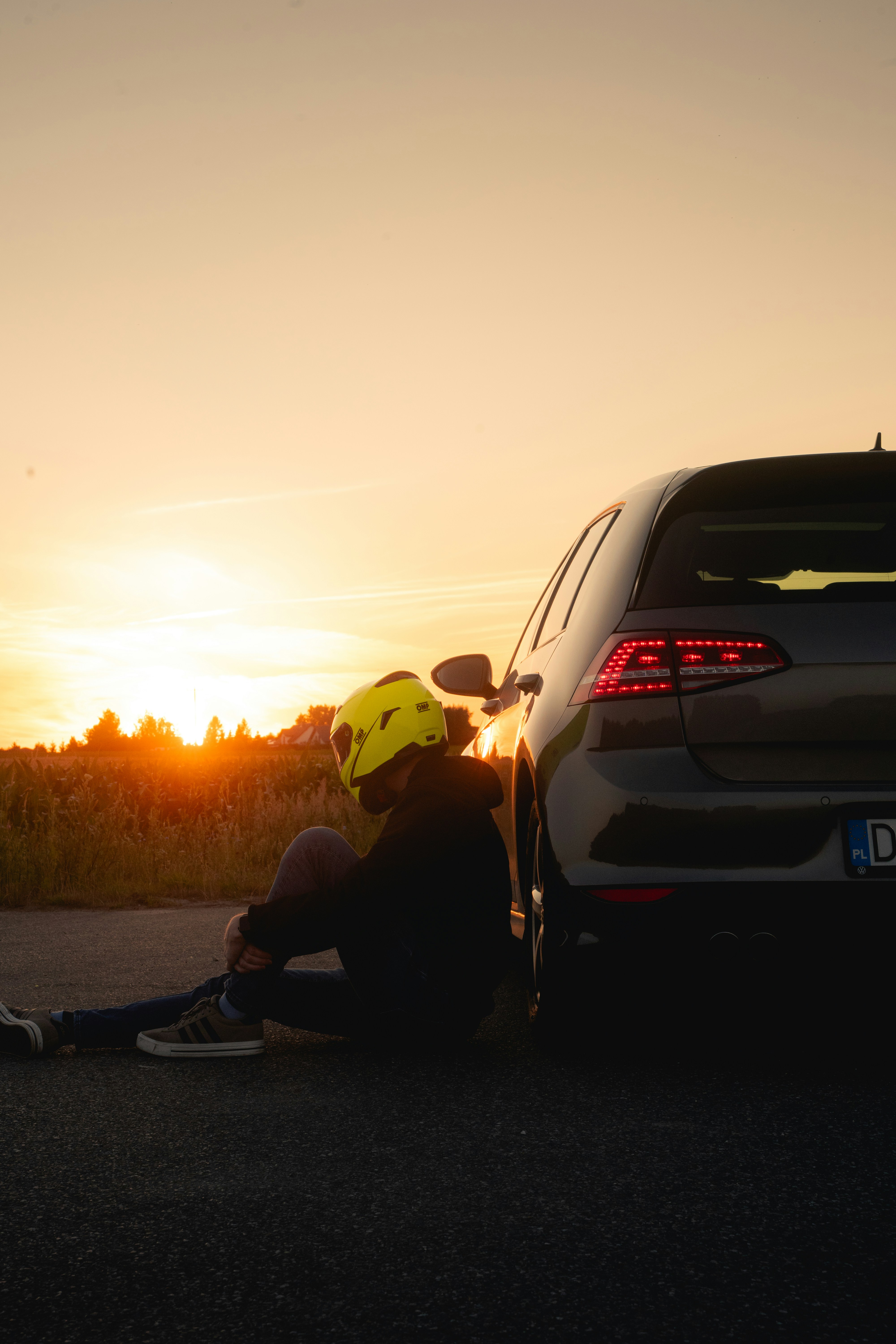 Person mit Helm sitzt bei Sonnenuntergang neben einem Auto.