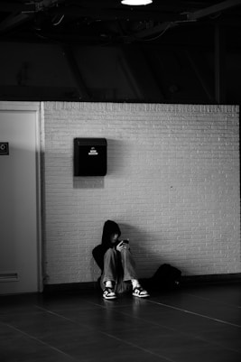 Person sits alone, head down, against the wall.