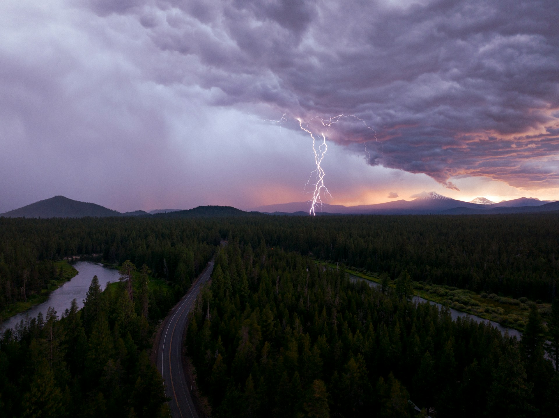Lightning strikes during a stormy evening over trees.