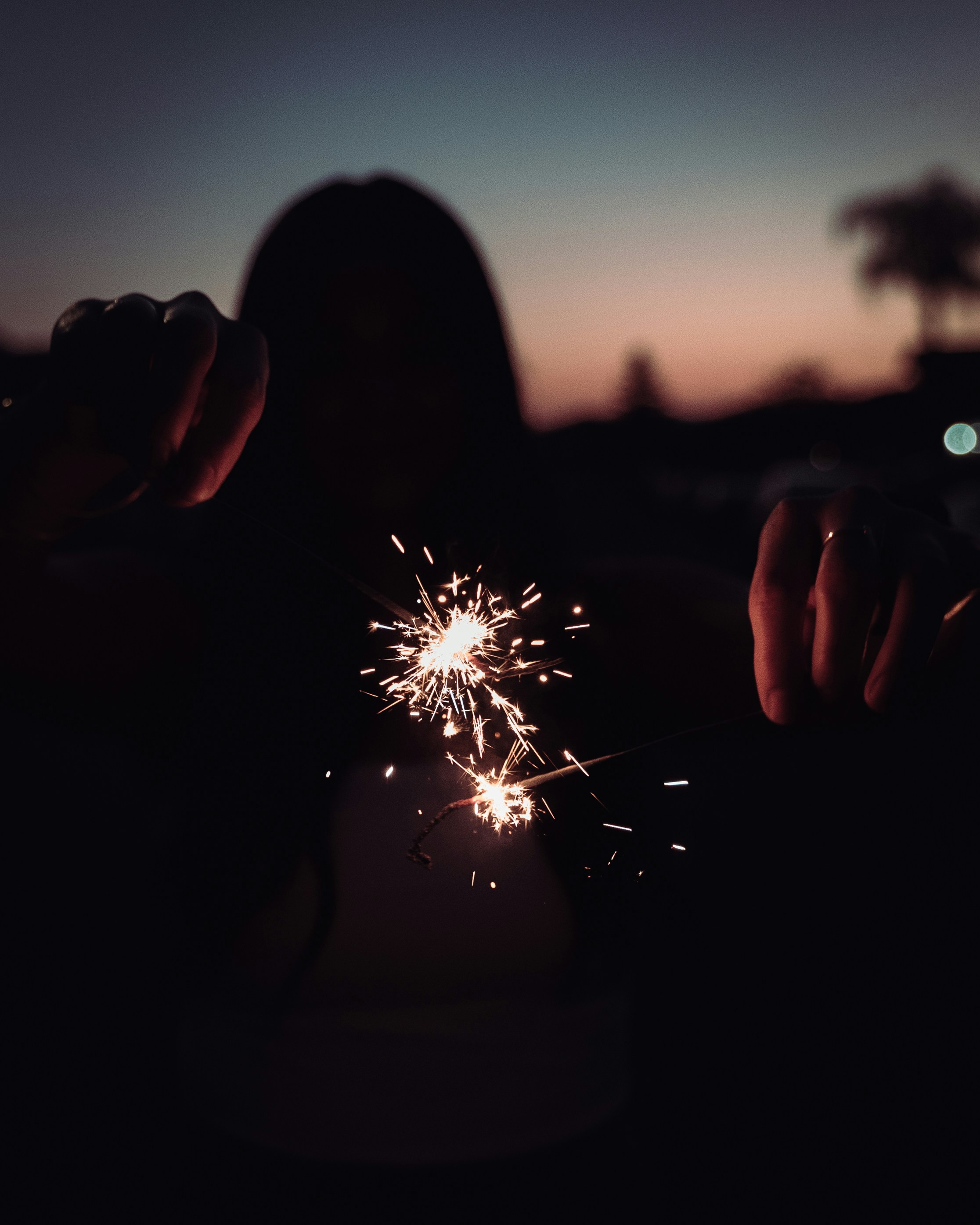 A person silhouetted with sparklers at dusk.