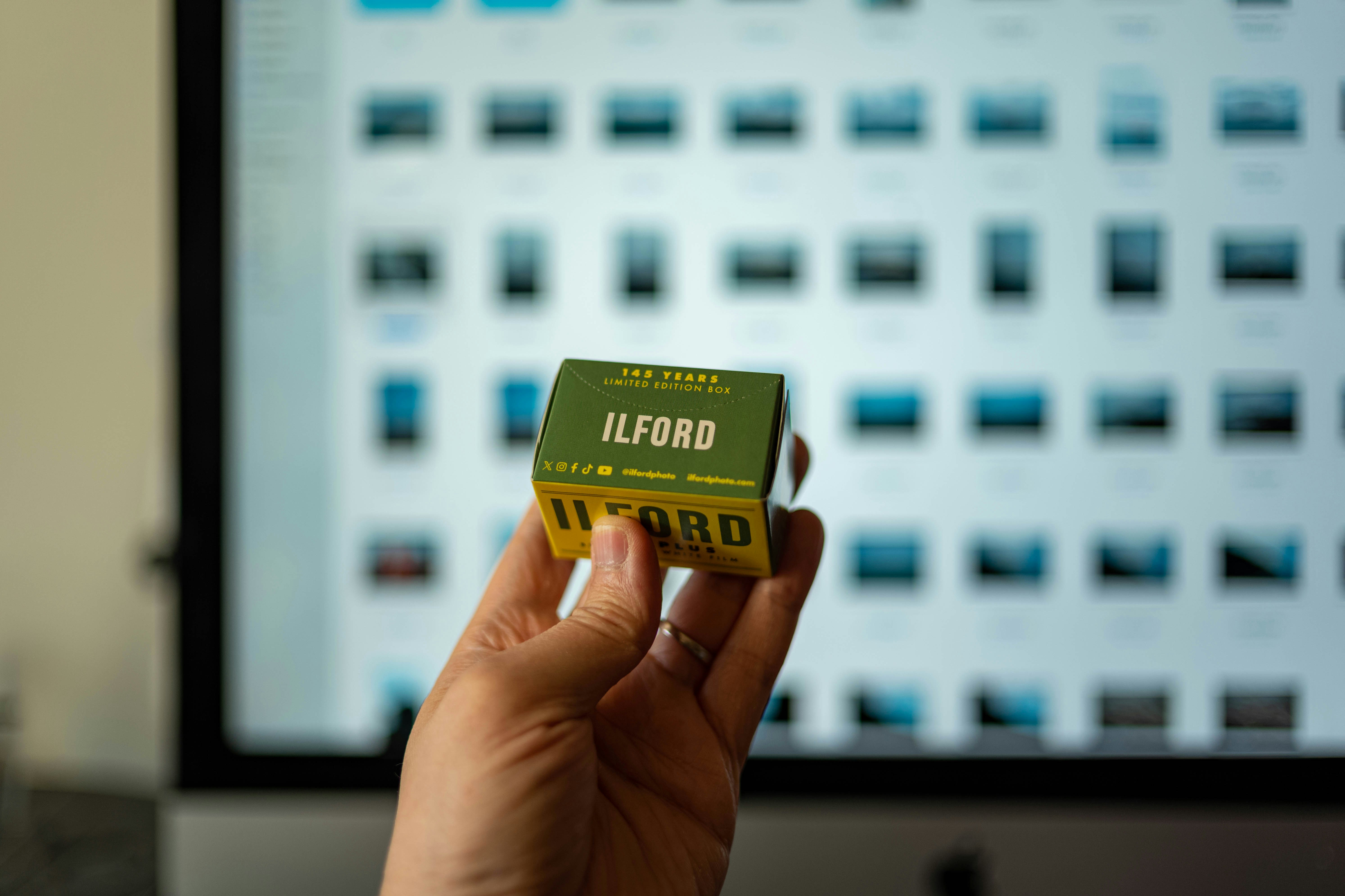 Hand holding ilford film with a computer in the background.