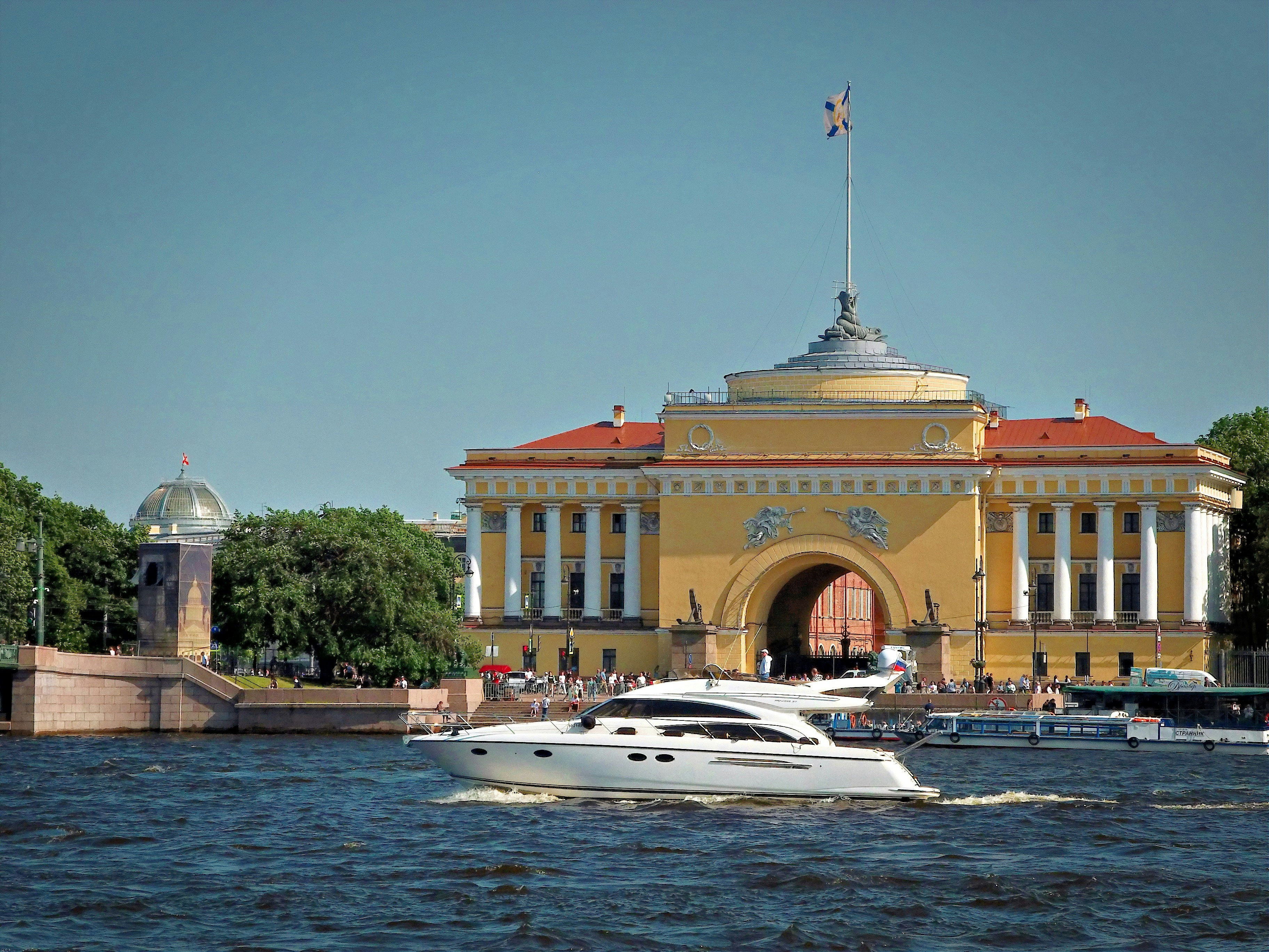 A yacht cruises past a scenic building.