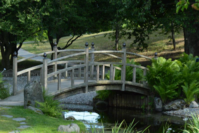 A wooden bridge arches over a serene pond.