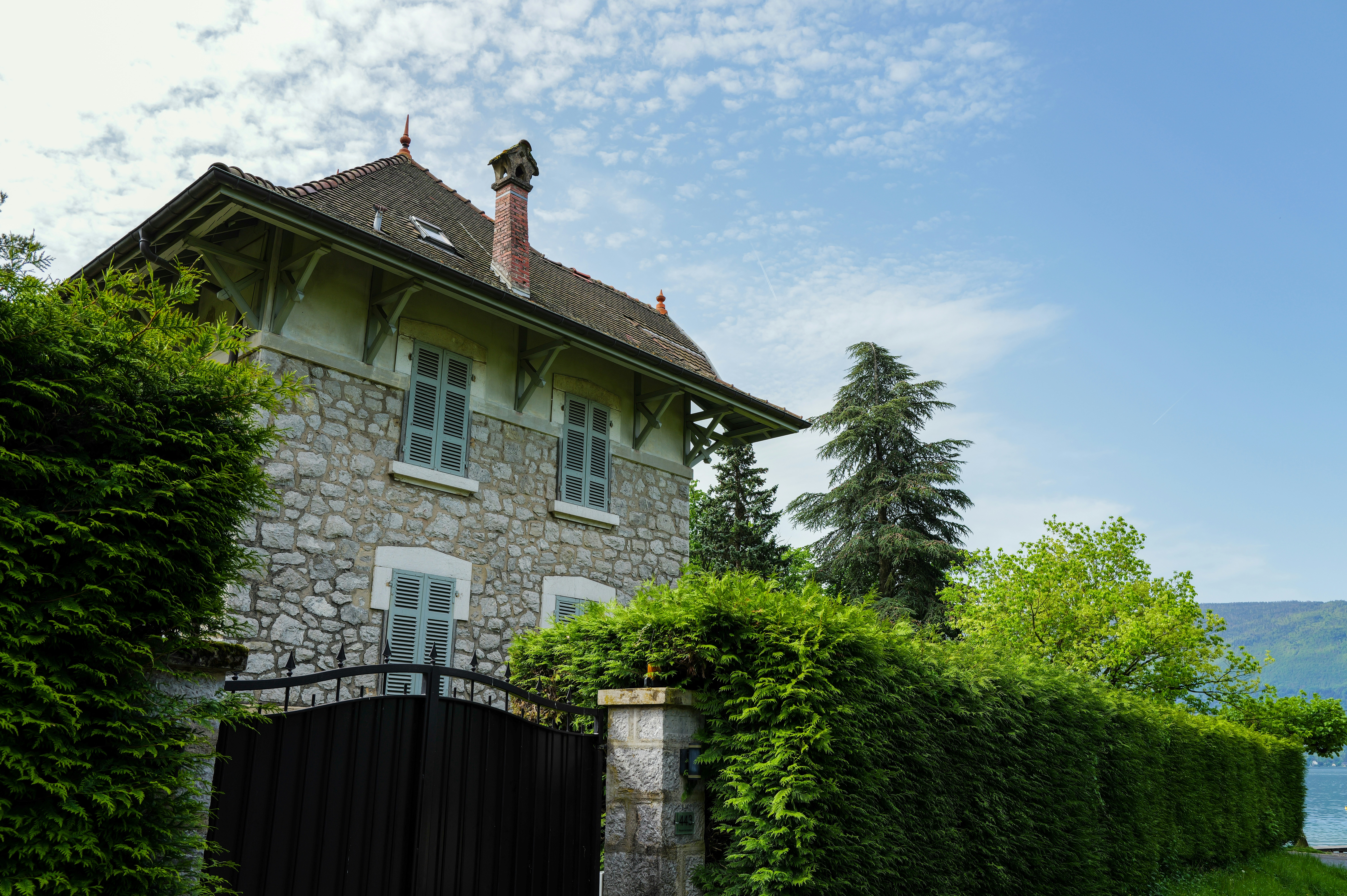 A stone house sits behind green hedges.