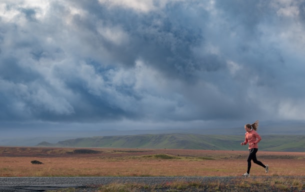 A woman runs outdoors under a cloudy sky.