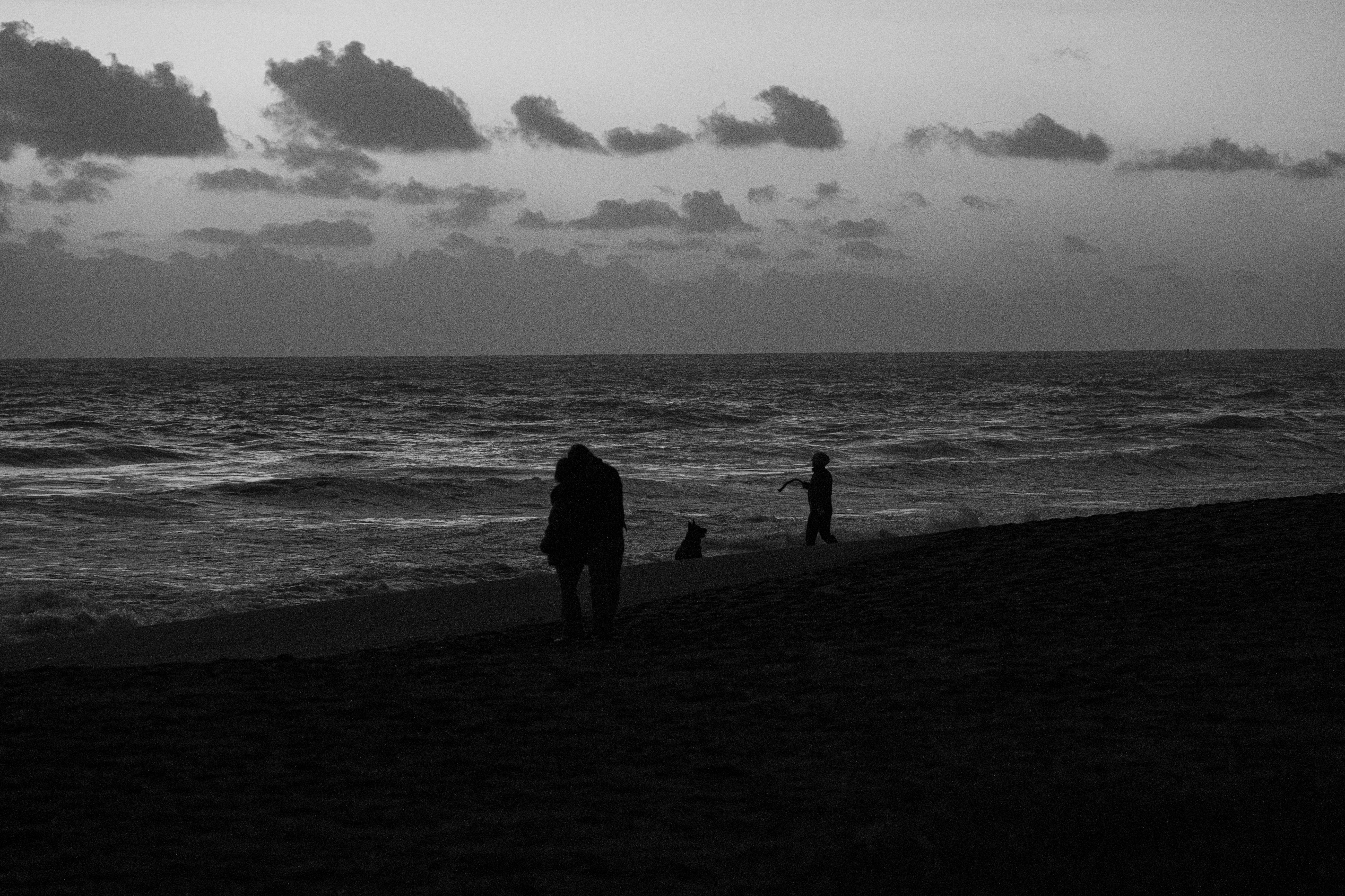 People walk on a beach during a moody sunset.