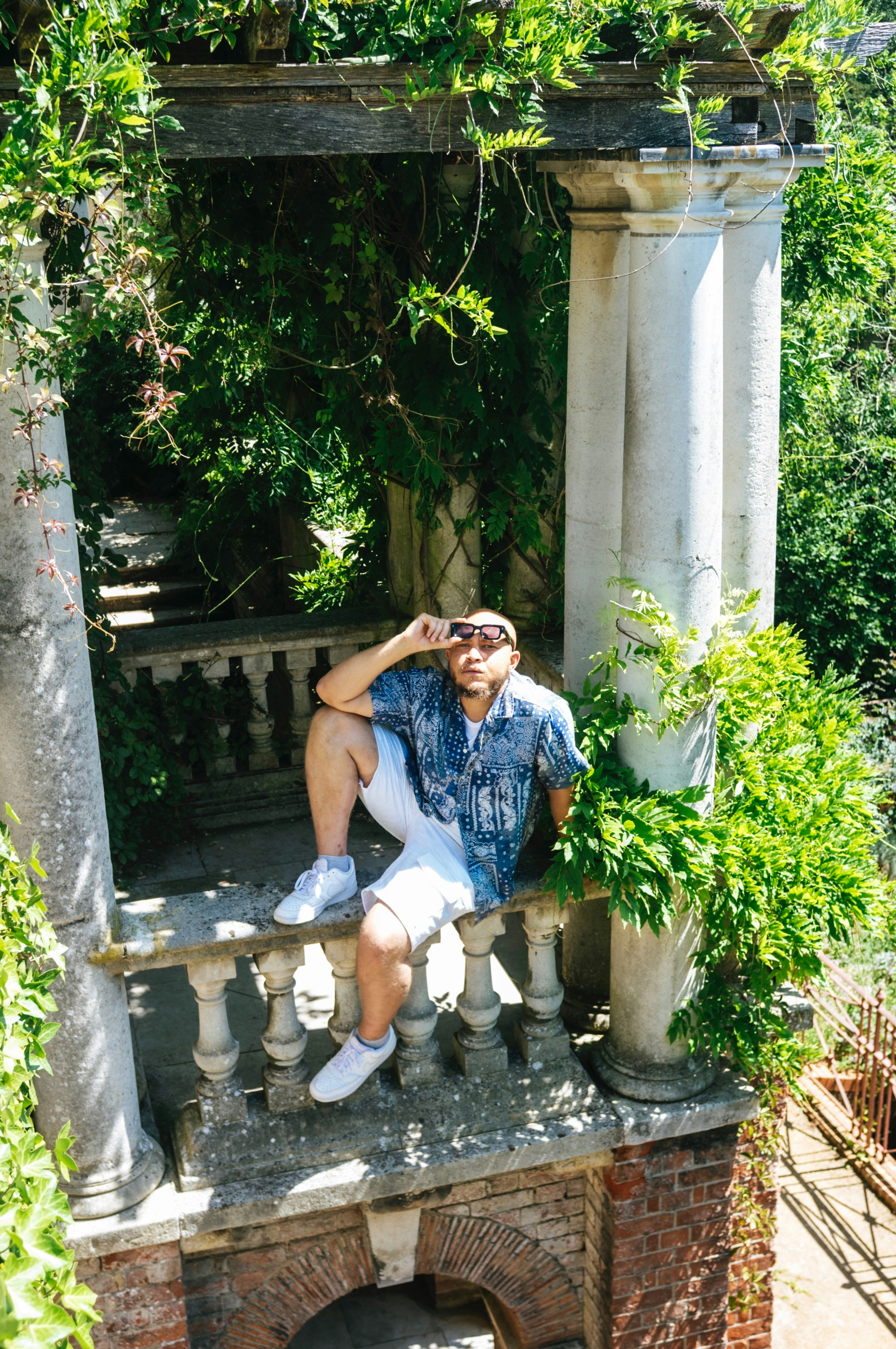 Man relaxing on a stone balcony surrounded by foliage.