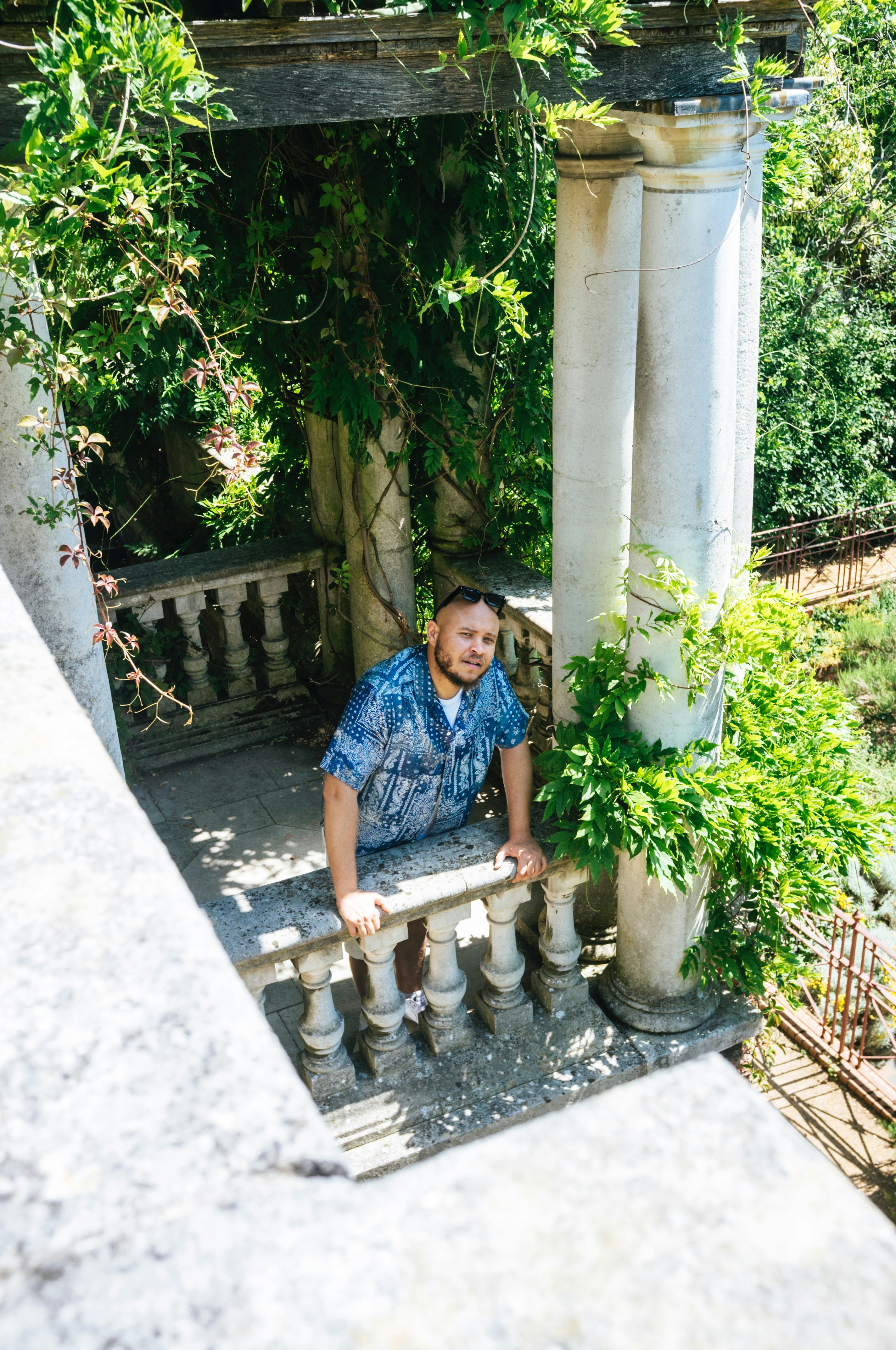 Man leans over a stone railing in a garden.