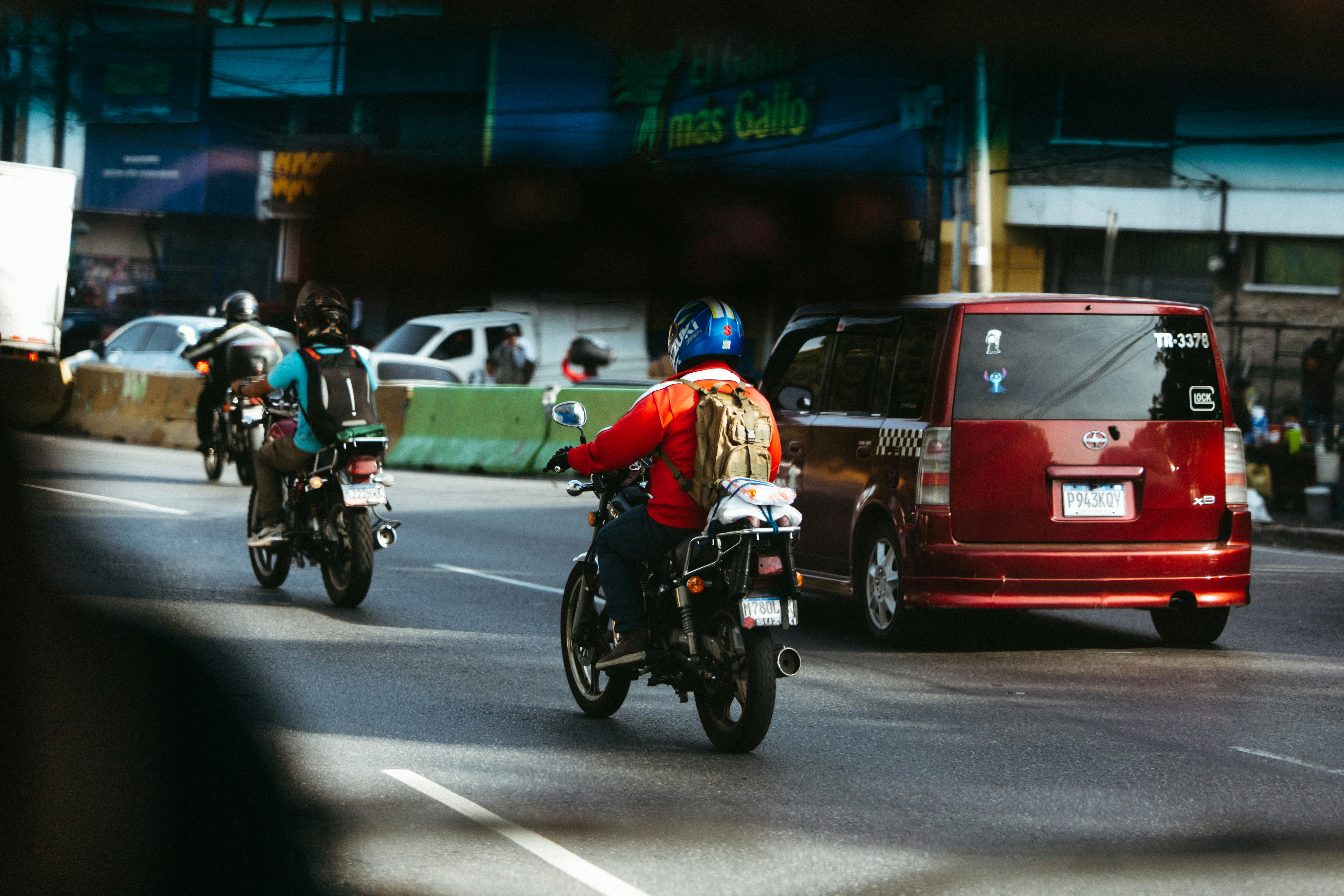Motorcyclists ride on a city street with a car.