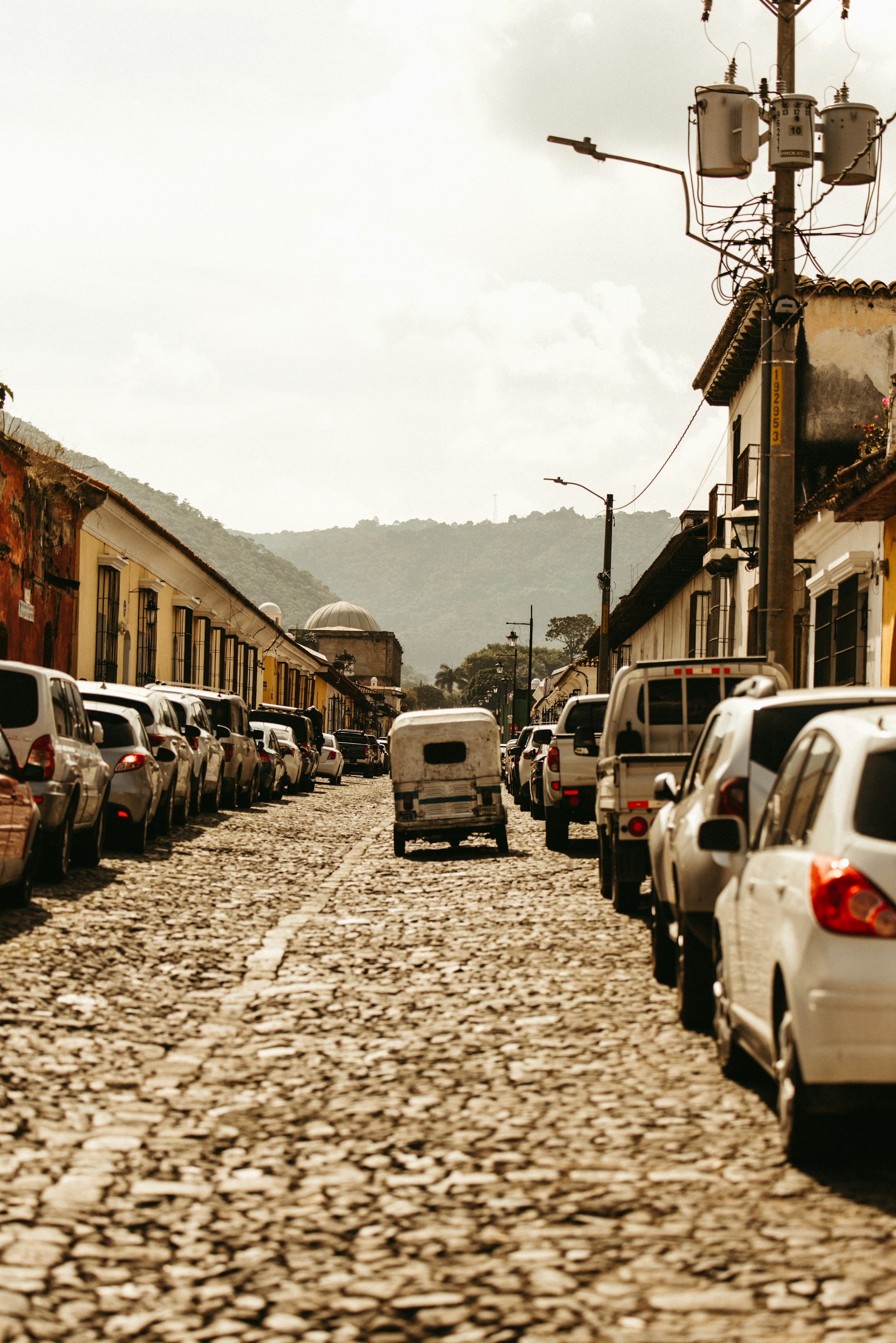 Cobblestone street lined with parked cars.