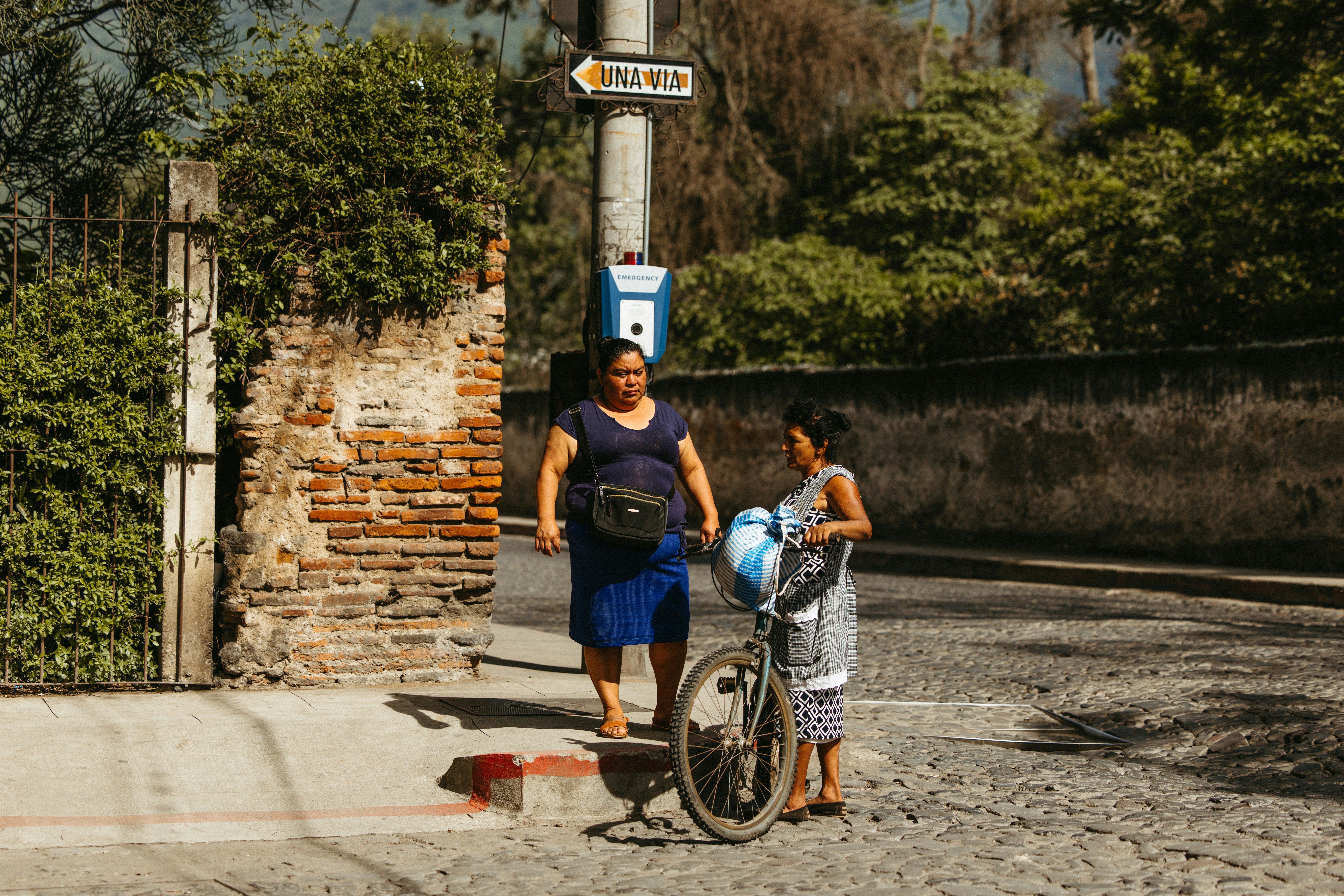 Two women stand on a cobblestone street with a bike.